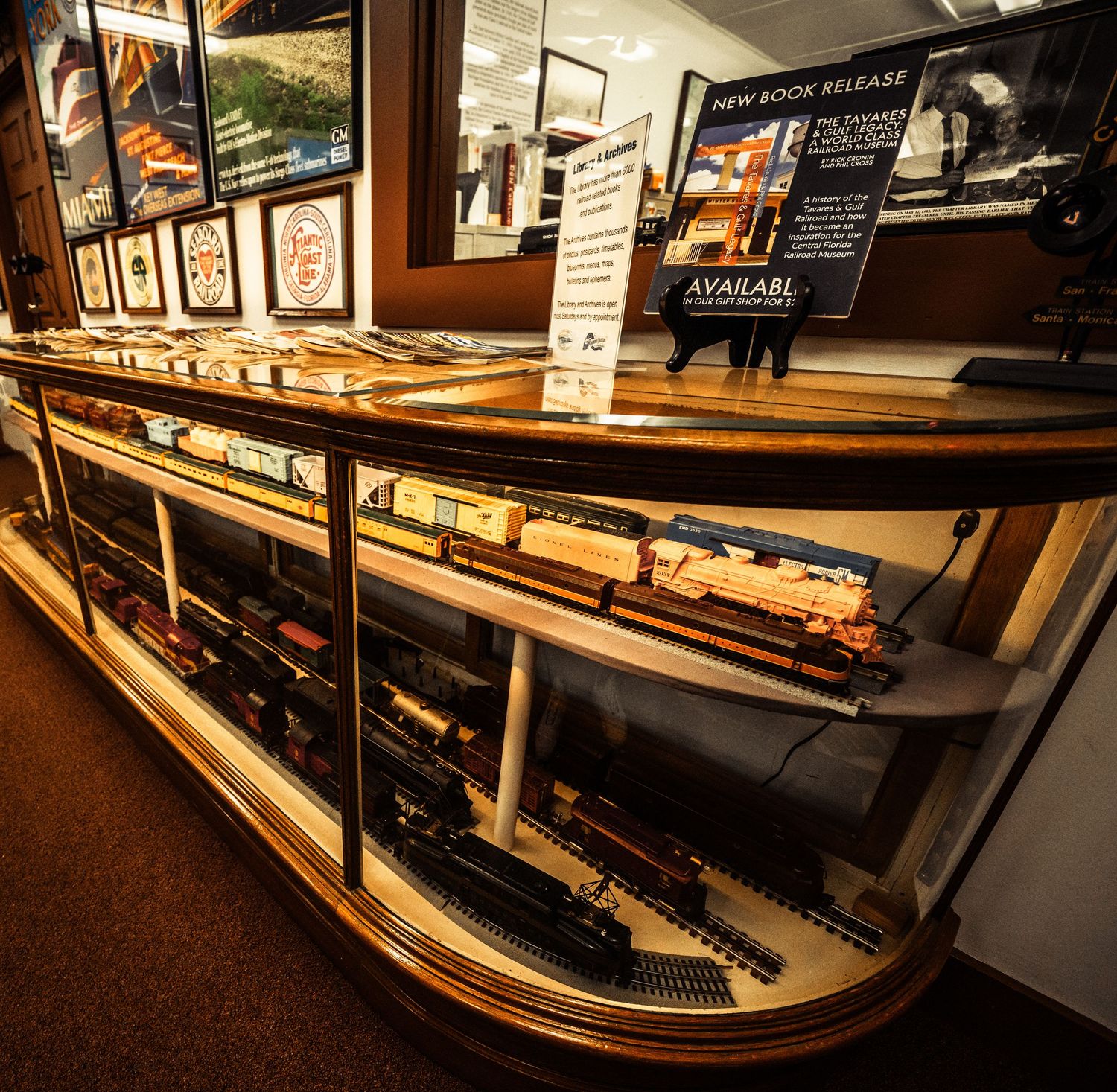 Panoramic view of model train layouts with curved tracks and detailed scenery under display lighting.