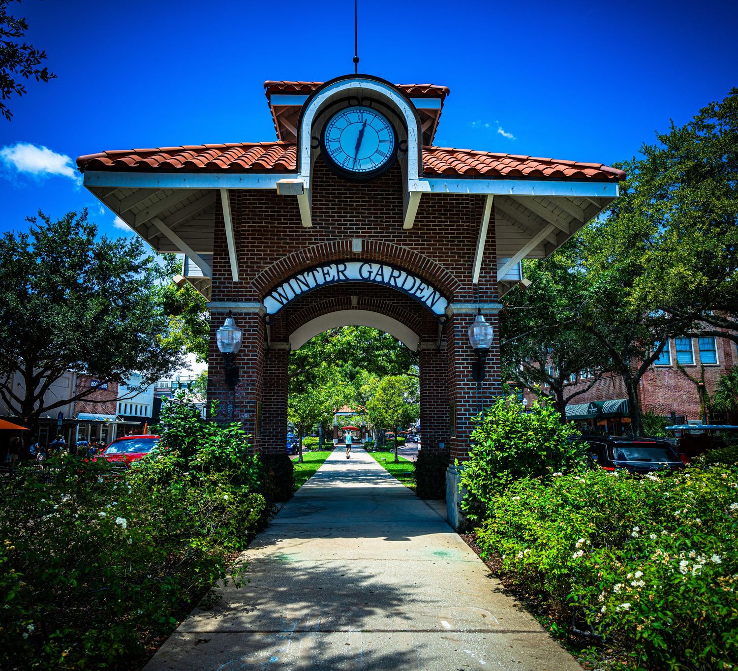 Brick archway entrance with Spanish tile roof and landscaping under bright blue sky.