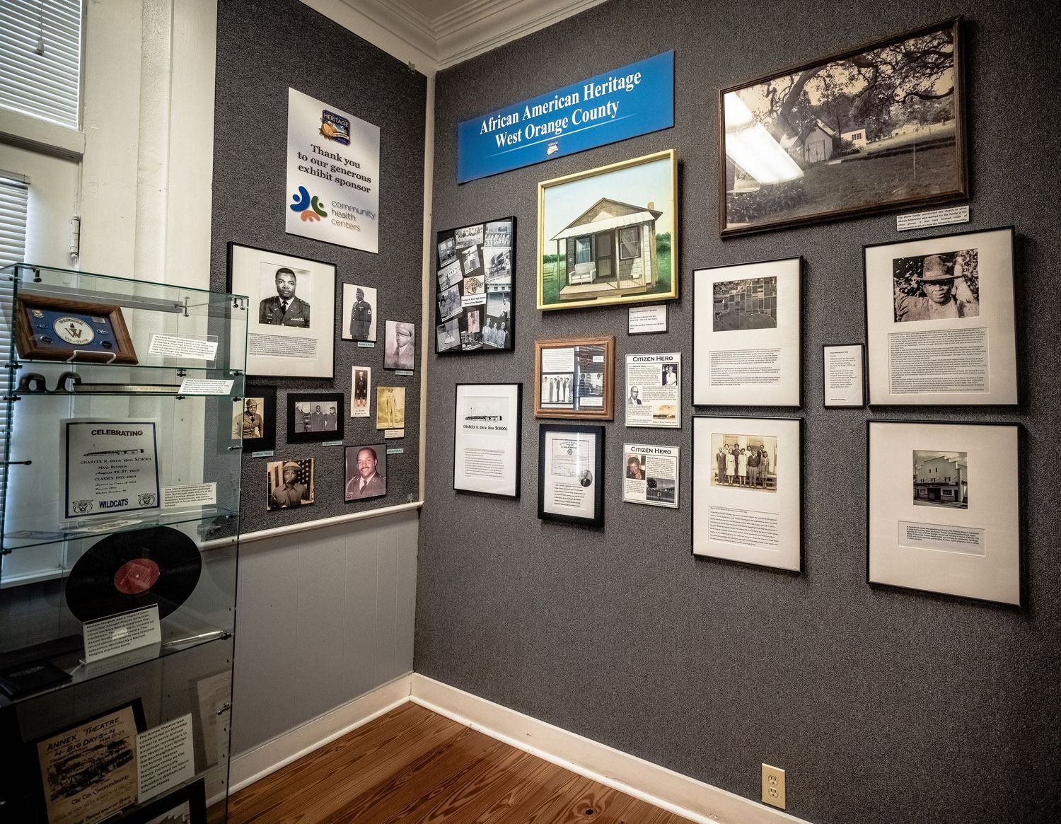 Museum exhibit room with historic photographs and documents displayed on dark gray walls.