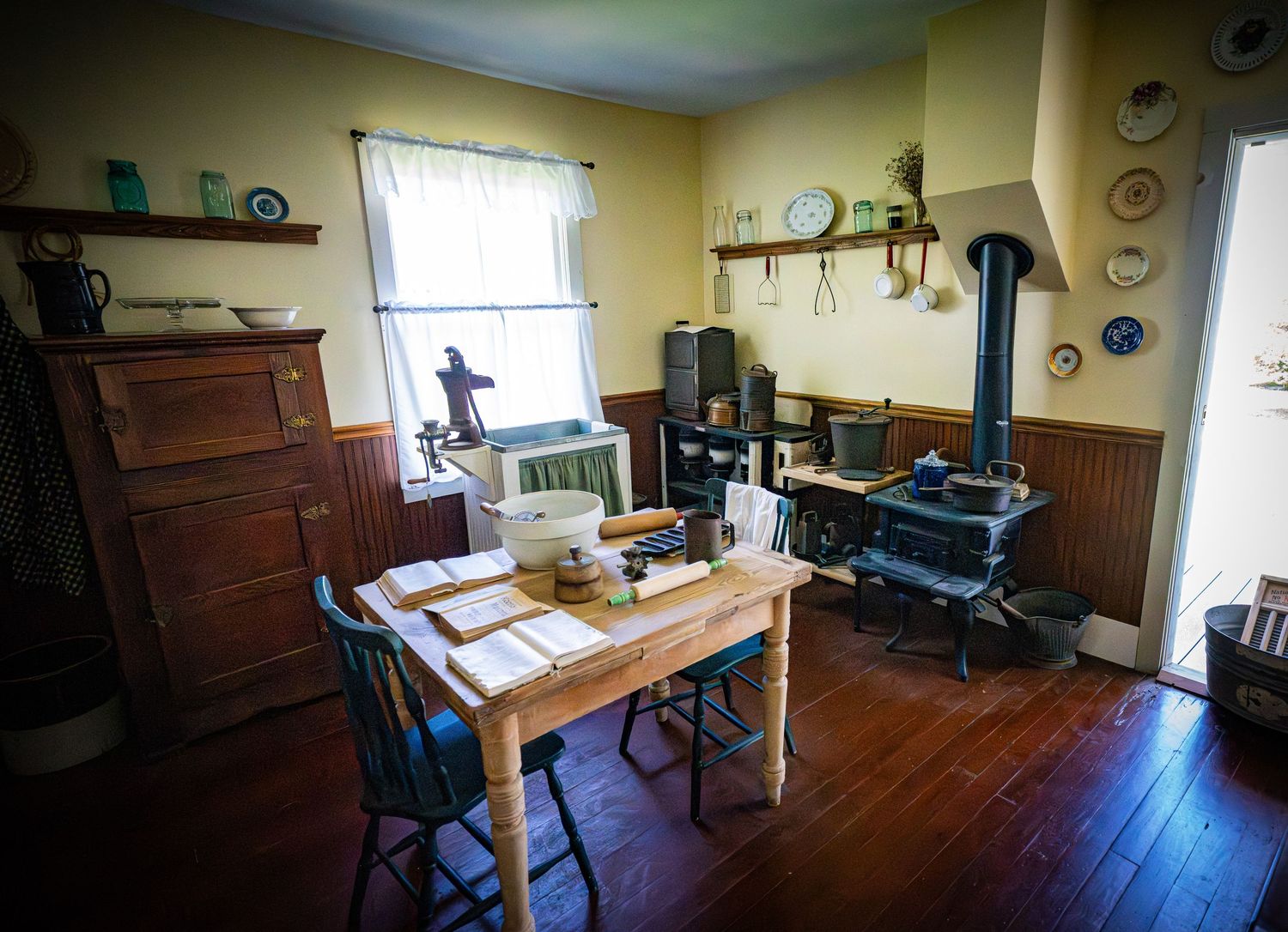 Historic kitchen with wood stove, wooden table, and period furnishings displaying vintage household items.