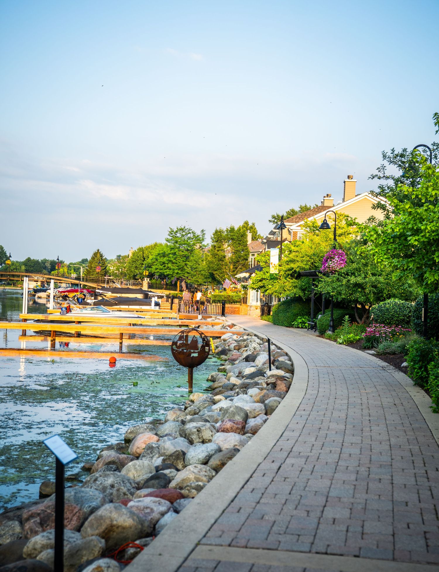 Curved brick promenade with ornamental lighting and rock barriers along a scenic waterfront.