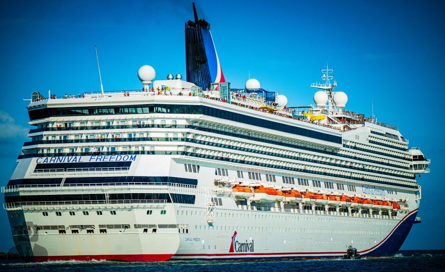 Luxury cruise ship with white exterior and multiple decks sailing across bright blue waters on a sunny day.