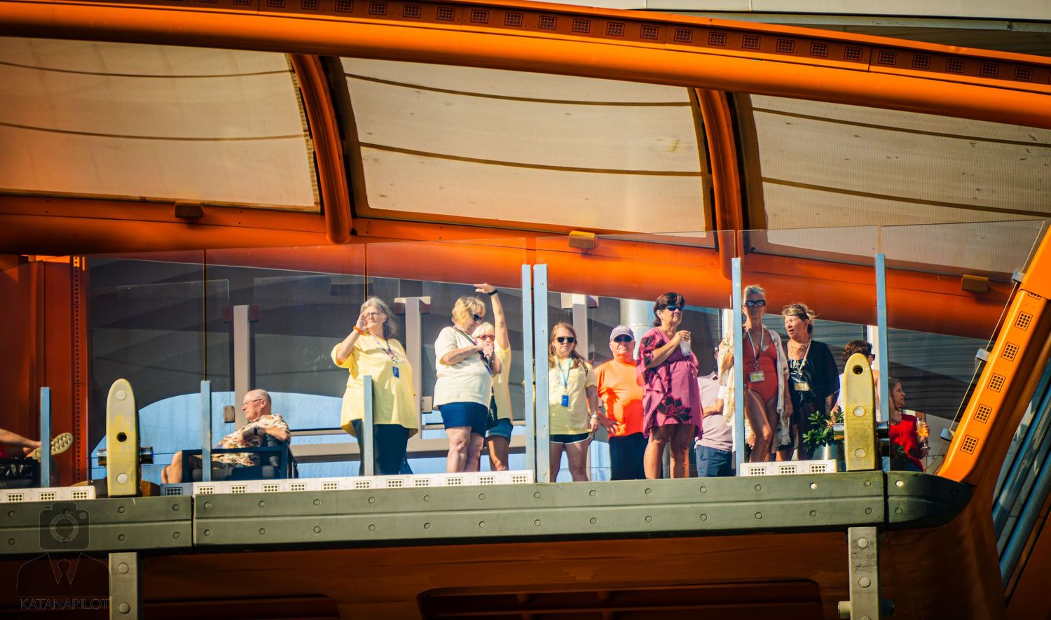 Silhouettes of people standing against an orange sunset sky through large windows in a modern building.