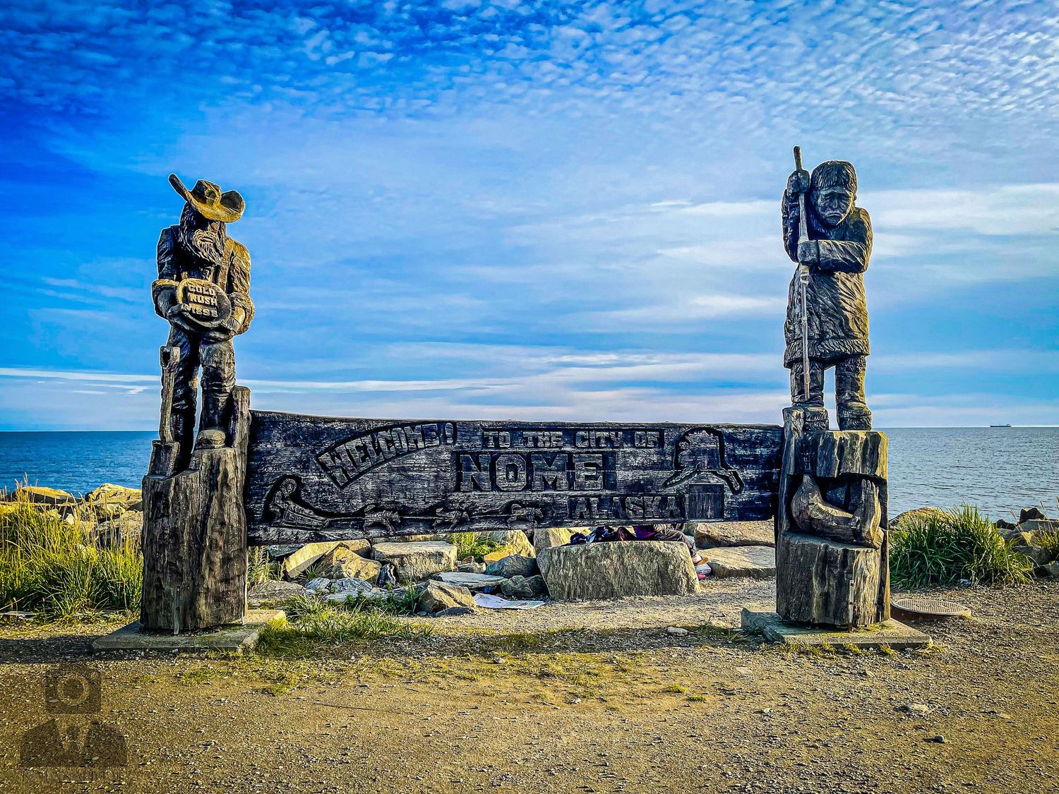 Wooden carved totems stand against a bright blue sky overlooking the ocean.