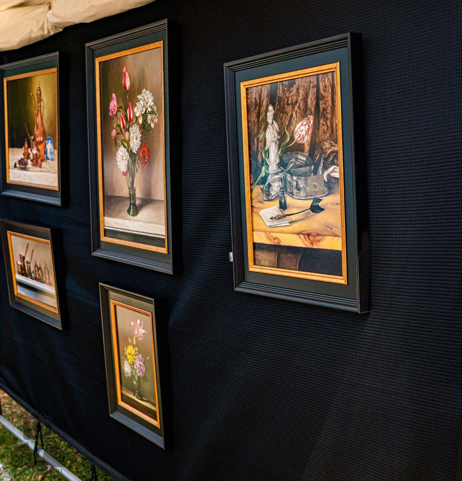 Art gallery wall displaying framed paintings in gold frames against a dark background.