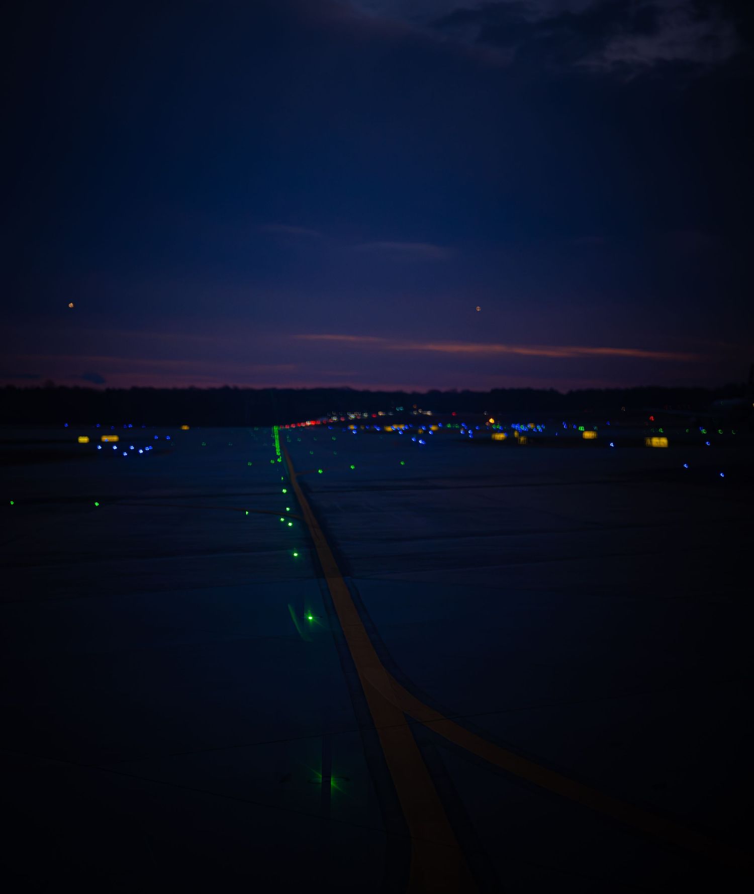 Panoramic view of an airport runway at night with glowing blue taxiway lights stretching into the dark horizon.