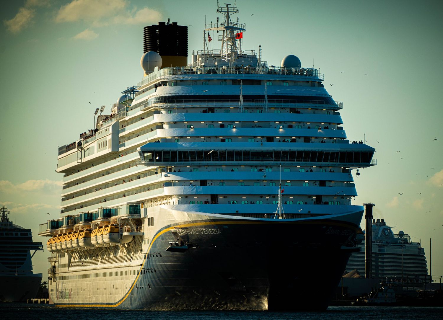 A panoramic series of luxury cruise ships docked at port during sunset with dramatic teal-tinted sky.