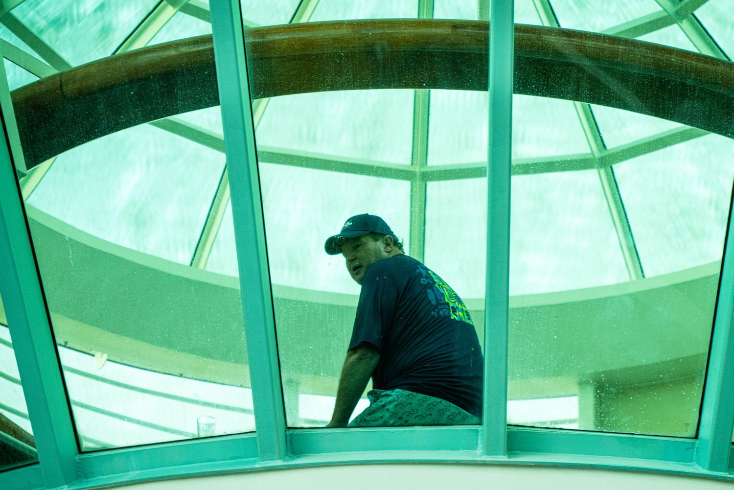 People gather in a modern glass-roofed atrium space with turquoise-tinted lighting and architectural elements.