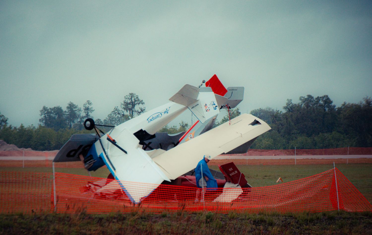 Closeup view of an overturned white airplane wreckage on a red clay surface at an airfield.
