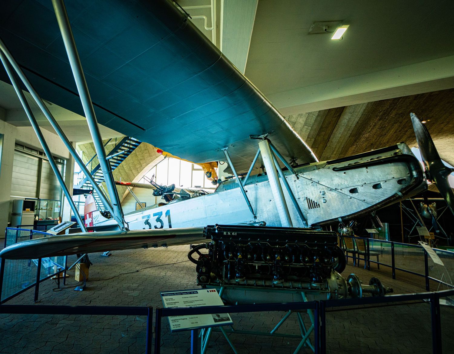 Vintage biplane marked 331 displayed in a museum hall, with an exposed radial engine and information placards in the foreground.