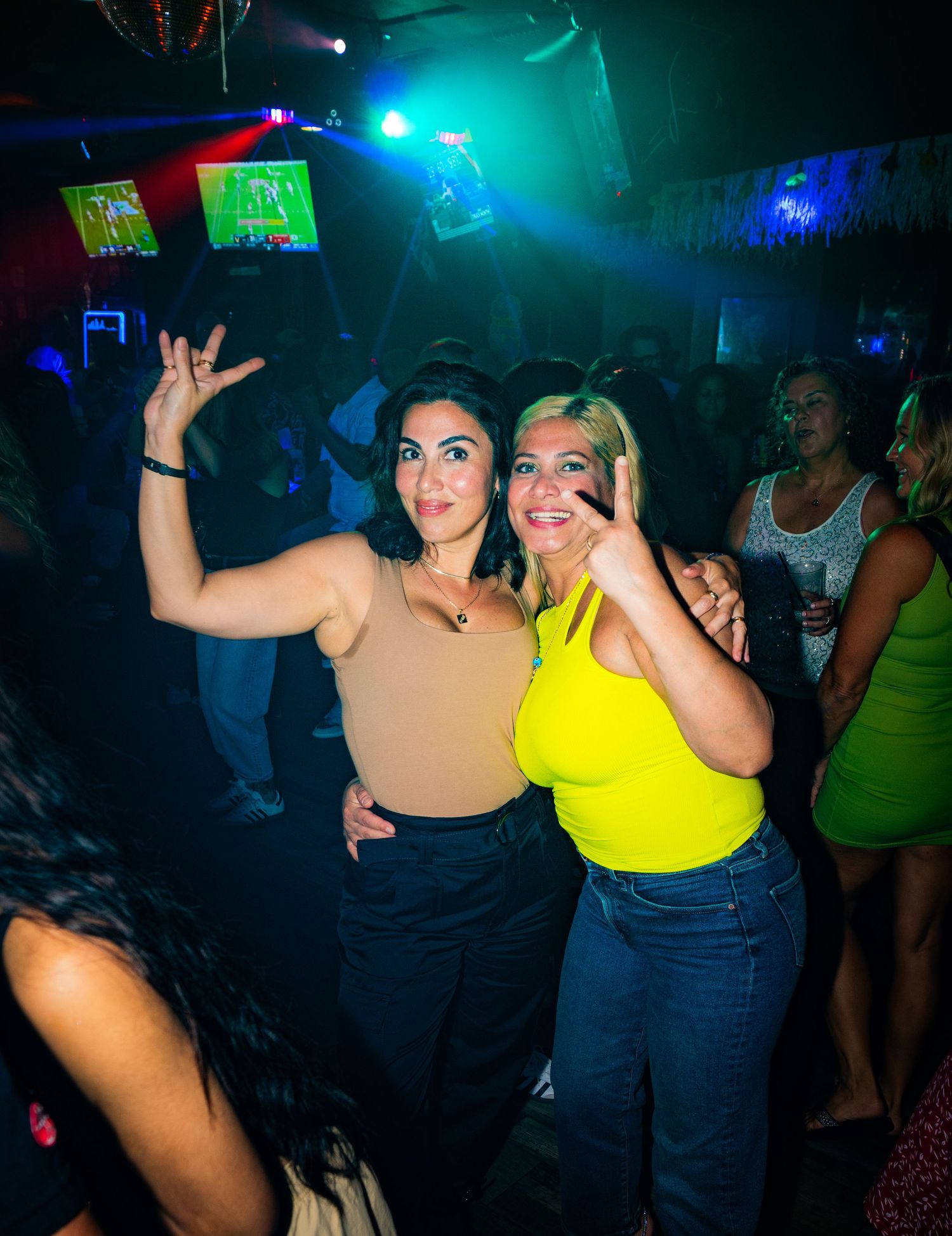 Friends dancing and posing together at a nightclub with colorful lighting effects.