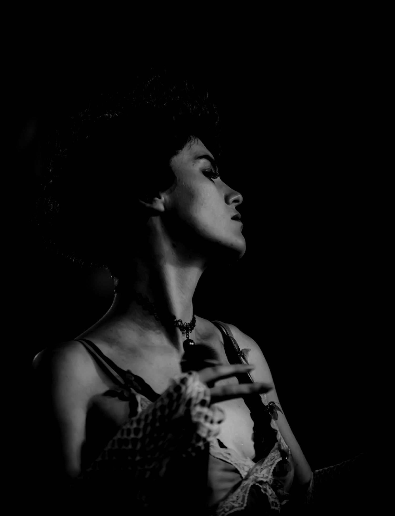 Black and white portrait of a woman looking upward in dramatic low-key lighting, wearing a delicate necklace.