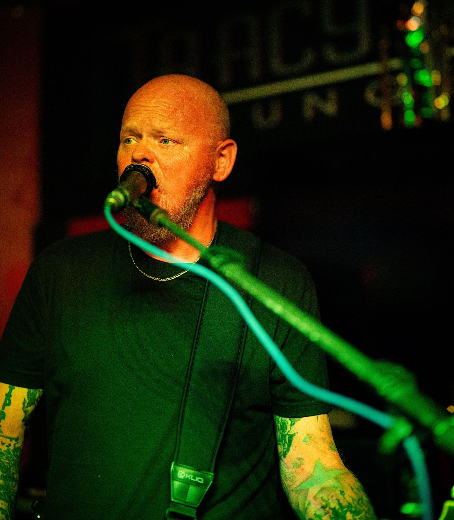 Vocalist performing with microphone under green stage lighting at music venue.