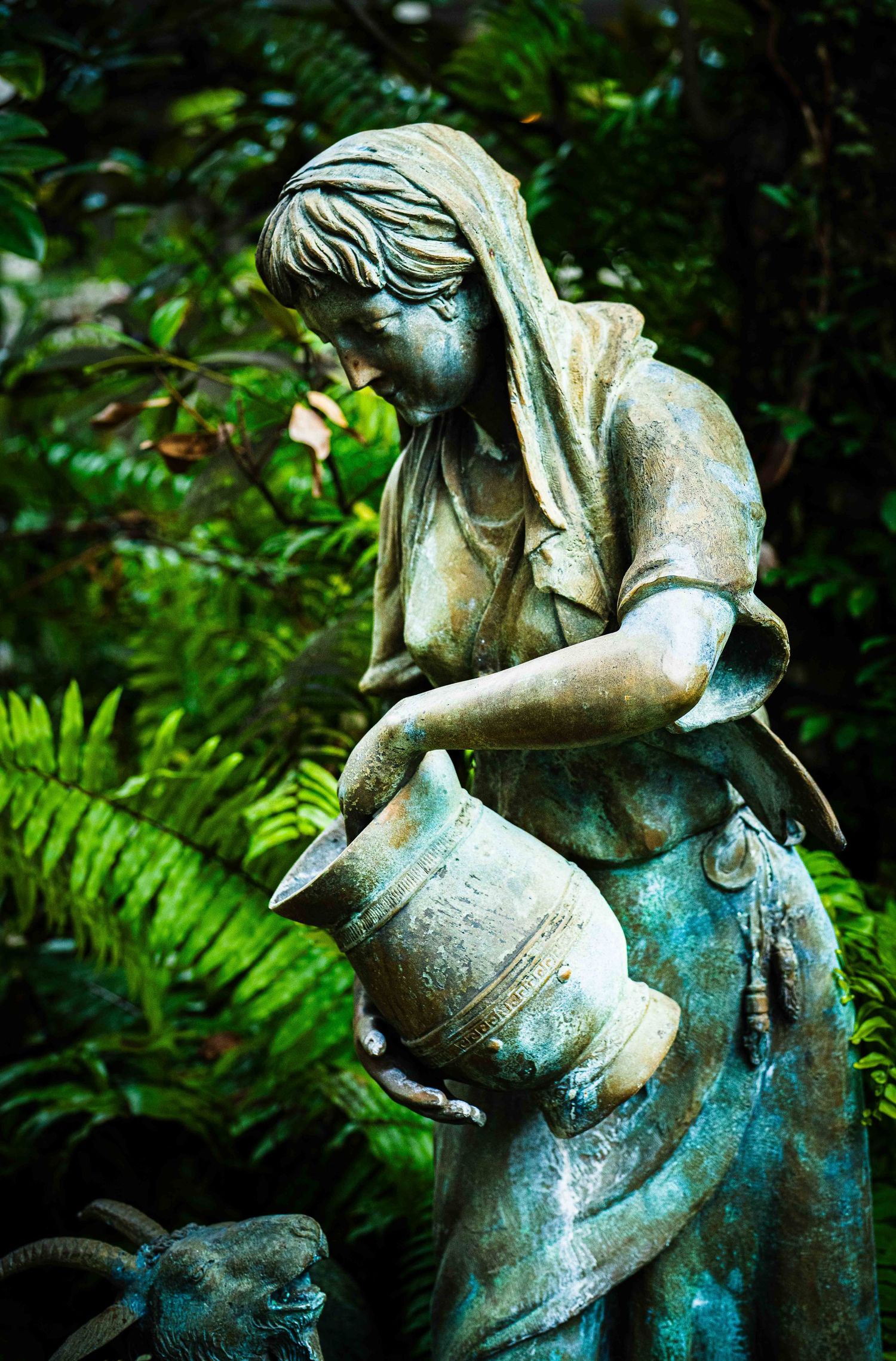 A sequence of garden statues depicting cherubs in weathered bronze patina among lush green foliage.