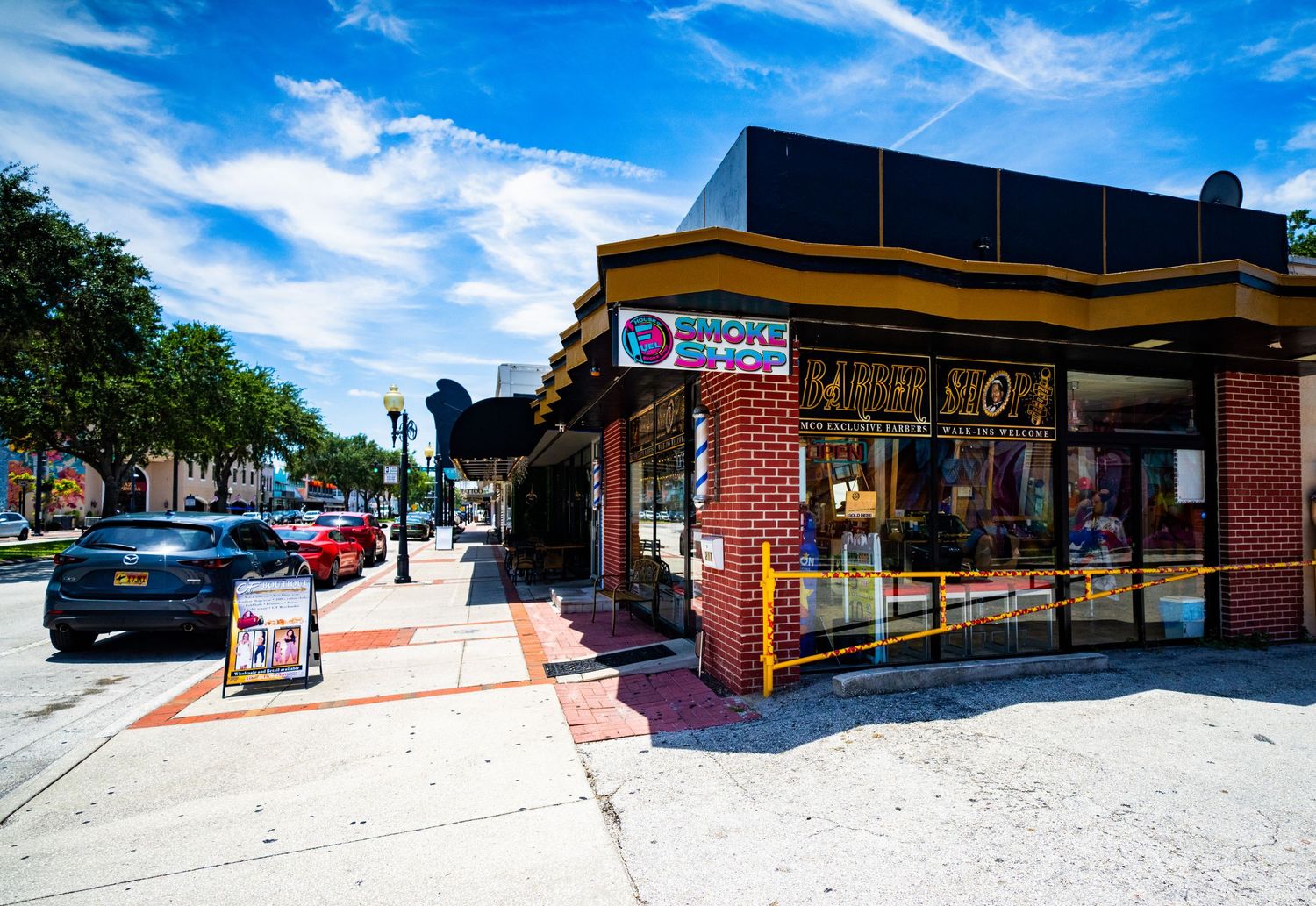 Strip mall exterior with brick facade and covered walkway under bright blue sky.