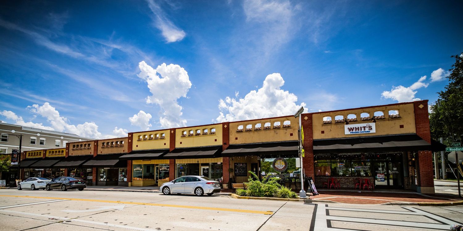 Strip mall style shopping center with brown brick facade and covered walkway on a sunny day.