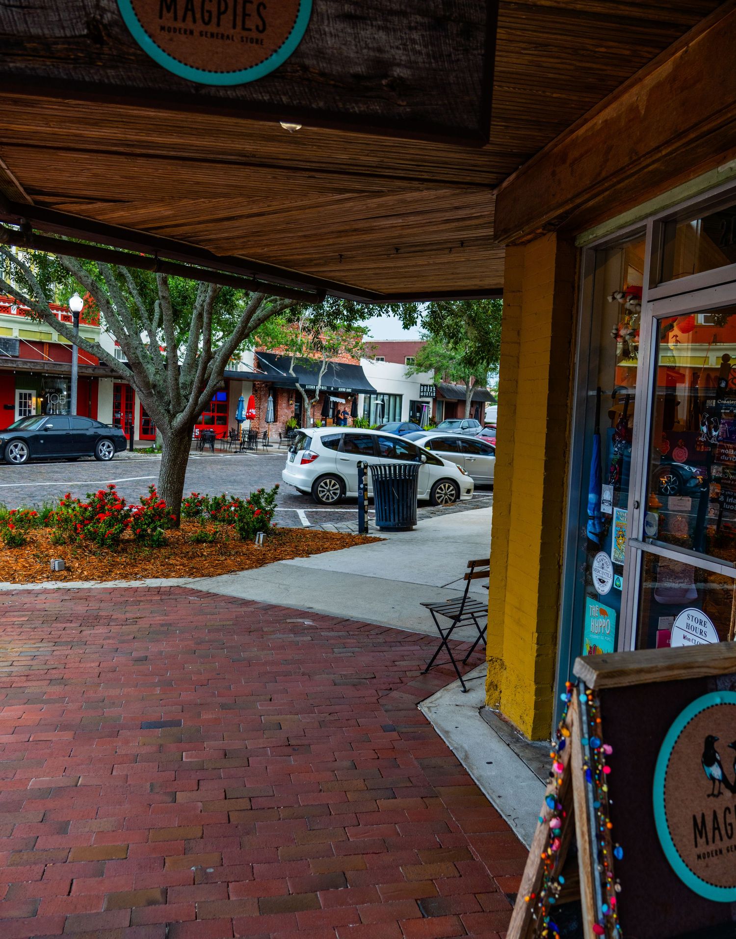 View of brick-paved sidewalk and storefronts from under a wooden awning in a shopping district.