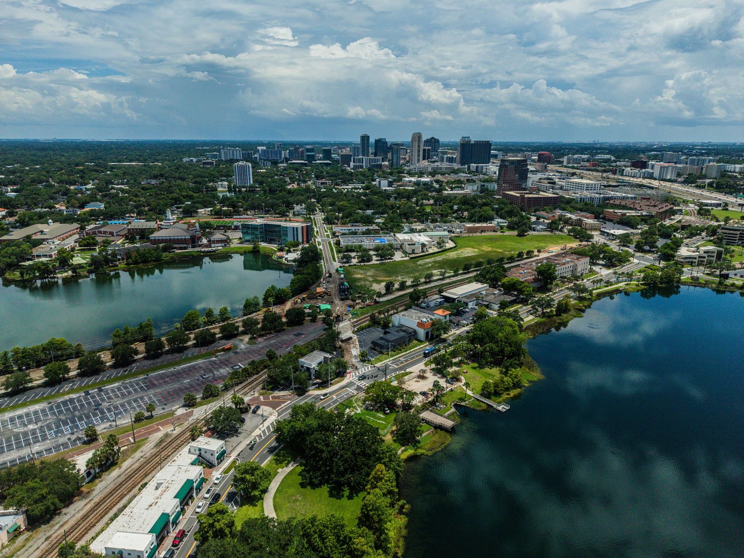Aerial view of Orlando, Florida skyline with lakes, lush greenery, and urban infrastructure under a cloudy sky.