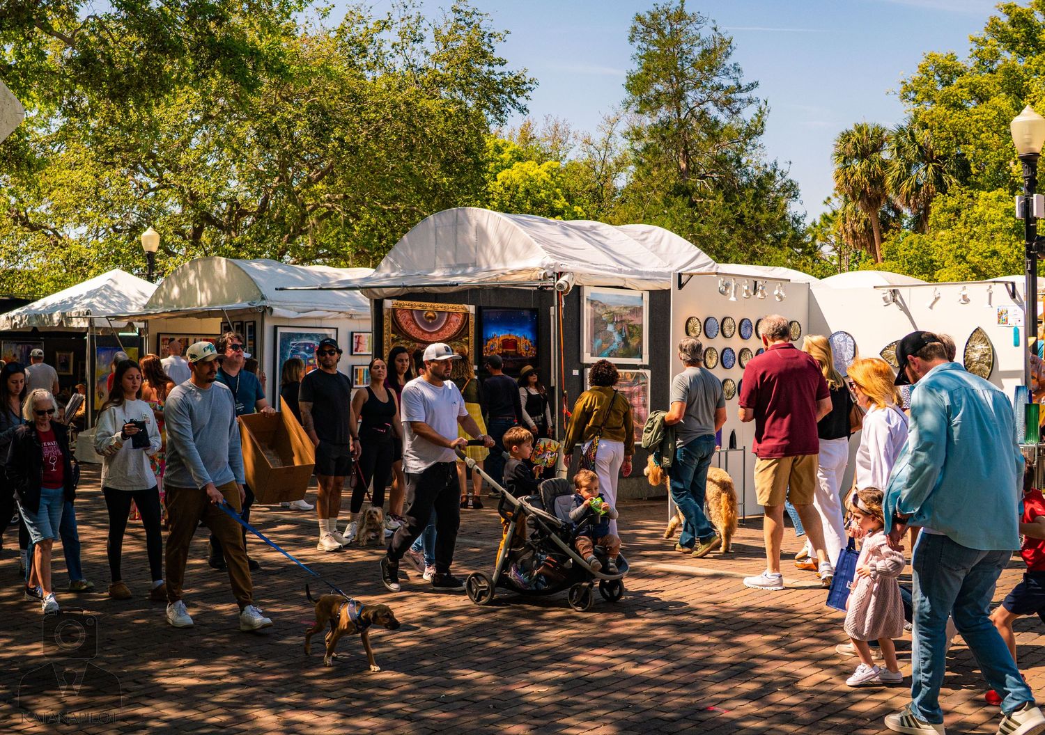 Outdoor art festival with white tents and crowds browsing vendor displays on a sunny day.