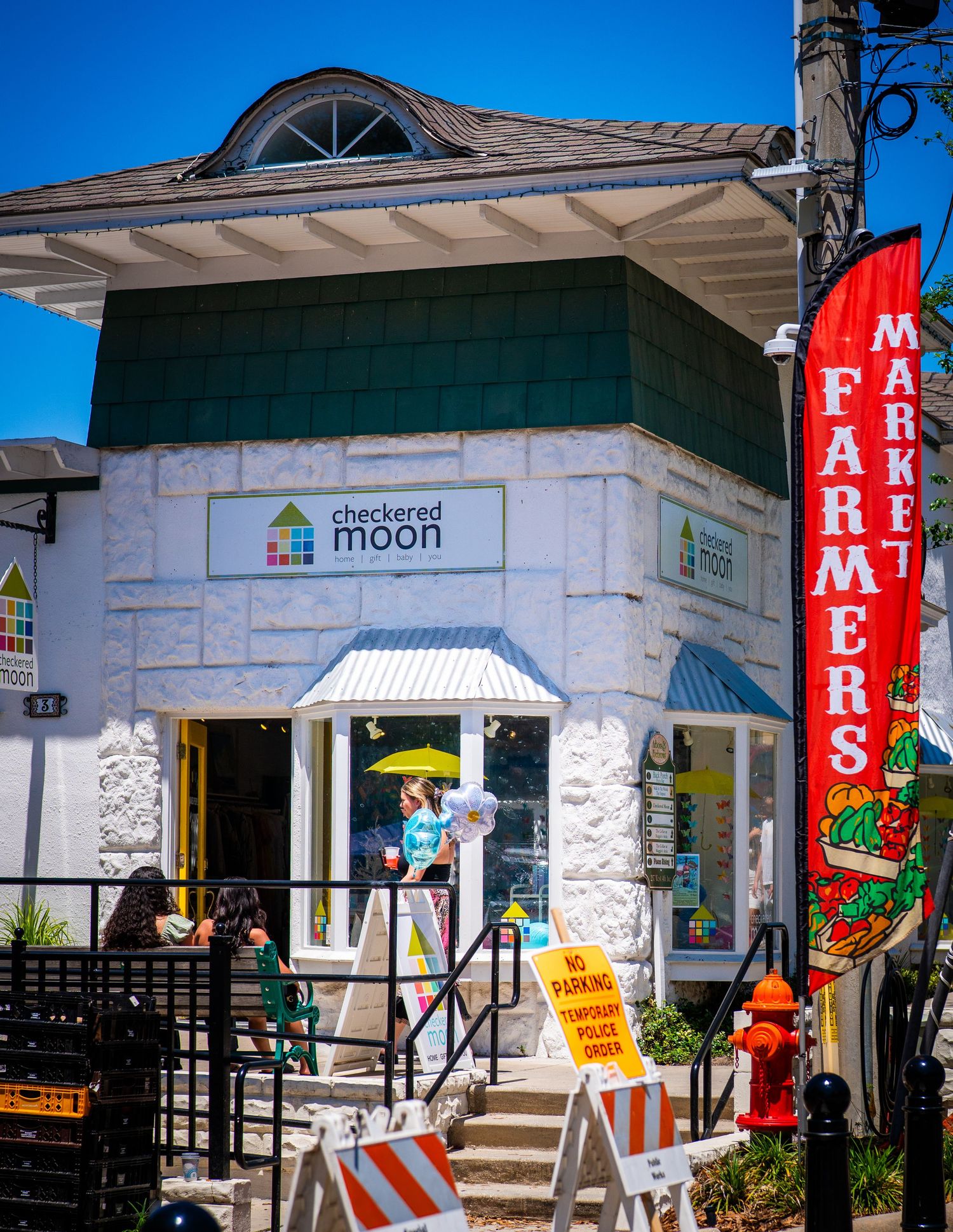 White stone building with green trim housing The Checkered Moon shop with Farmers Market sign.
