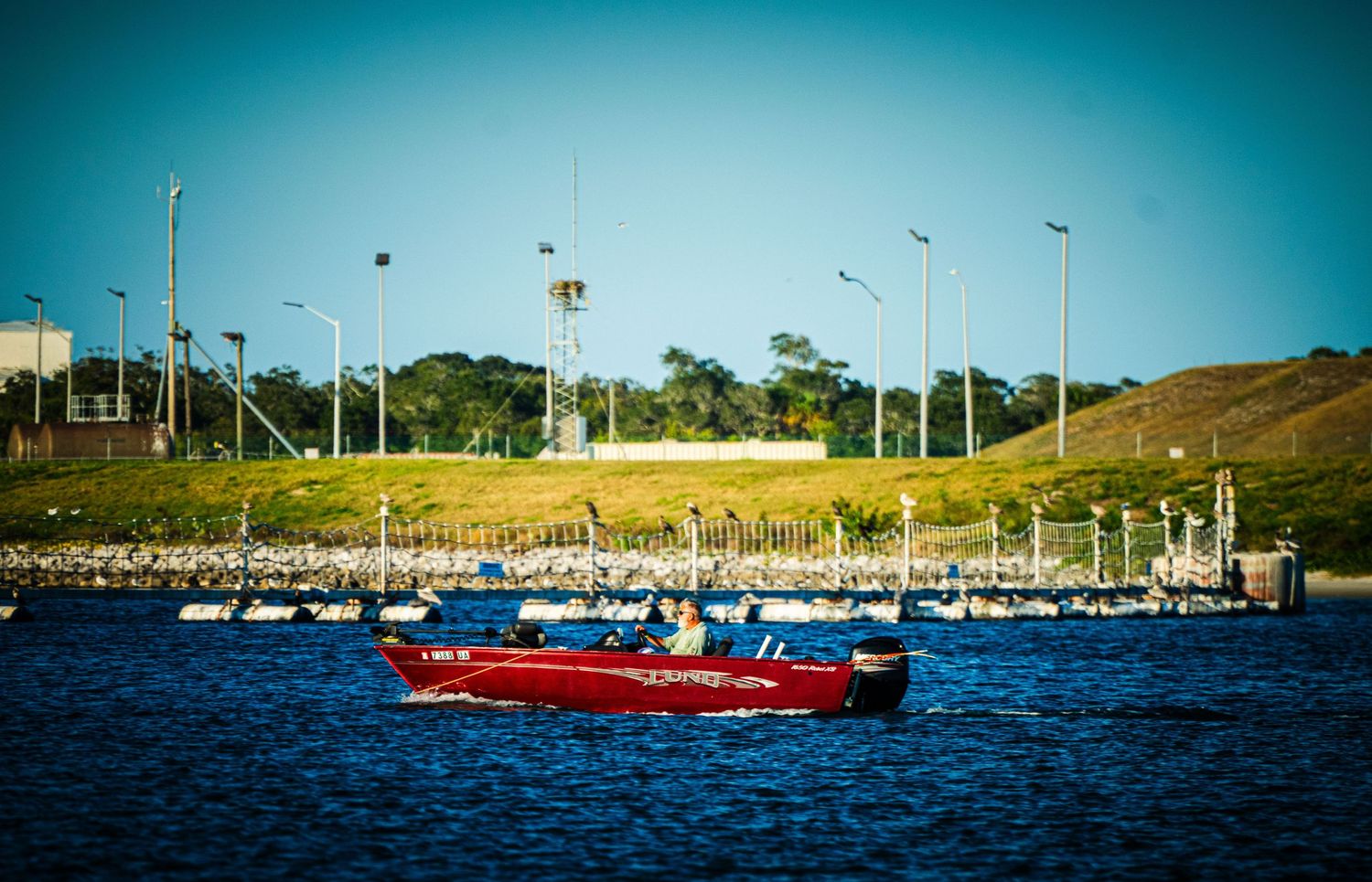 A panoramic view of sailboats moored in a marina with blue water and a turquoise sky on a sunny day.