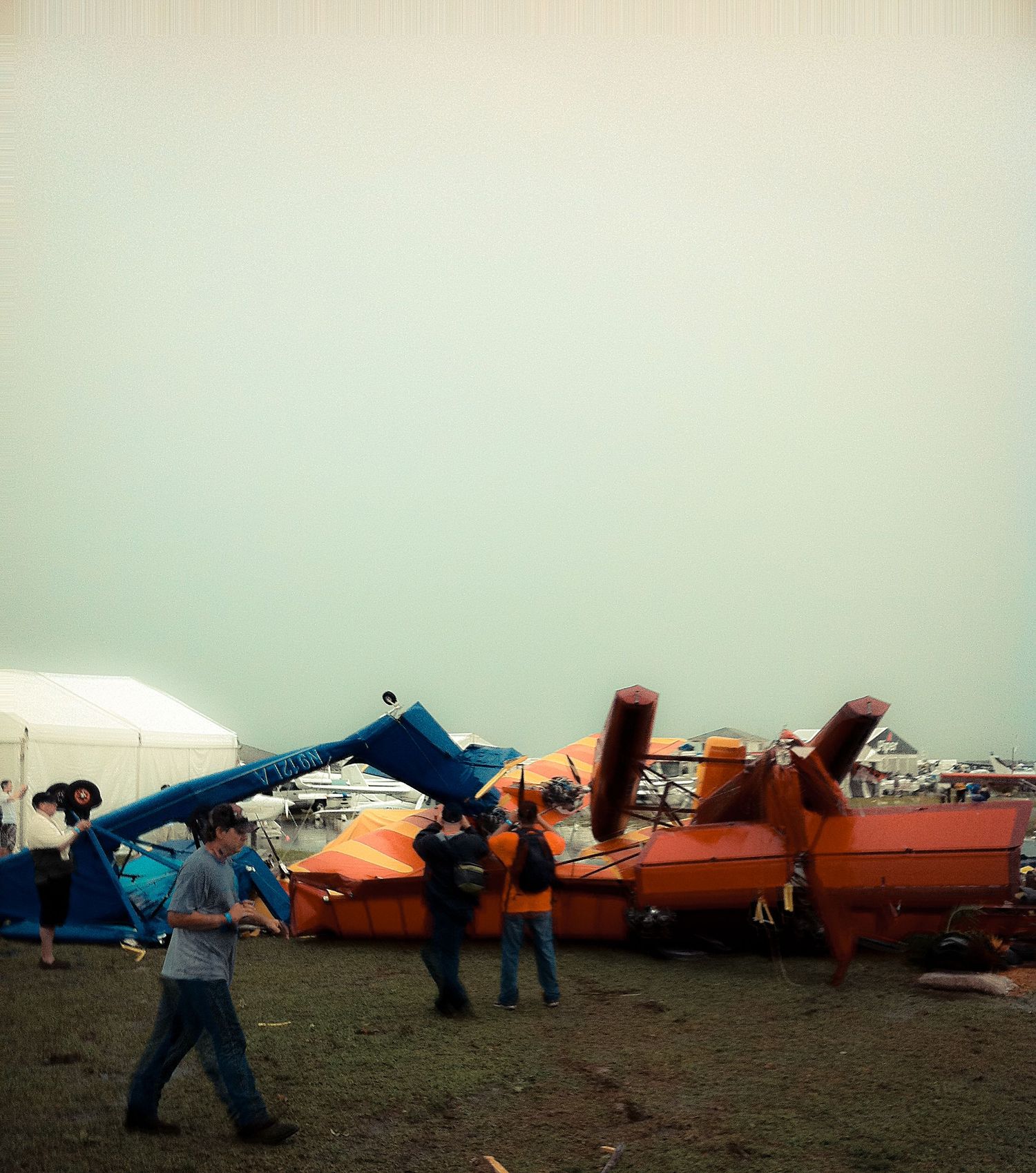 Several damaged aircraft and debris scattered on a field after what appears to be storm or disaster damage.