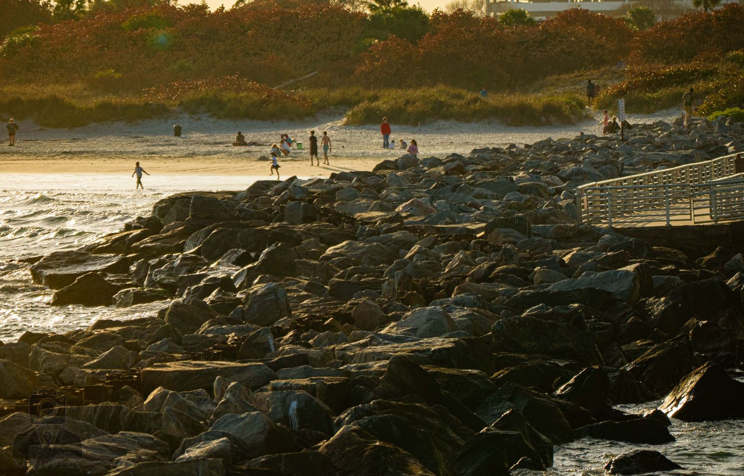 Rocky coastline with waves crashing against dark volcanic rocks during sunset at a beach.