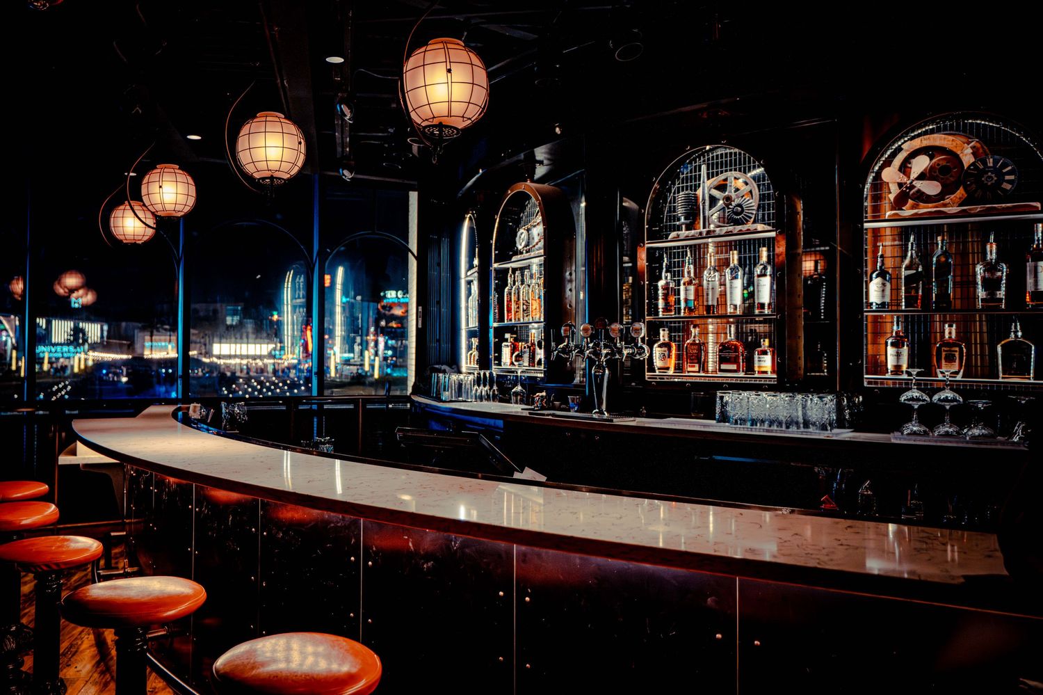 Modern bar interior with glowing paper lanterns and red bar stools creating a warm, atmospheric ambiance.