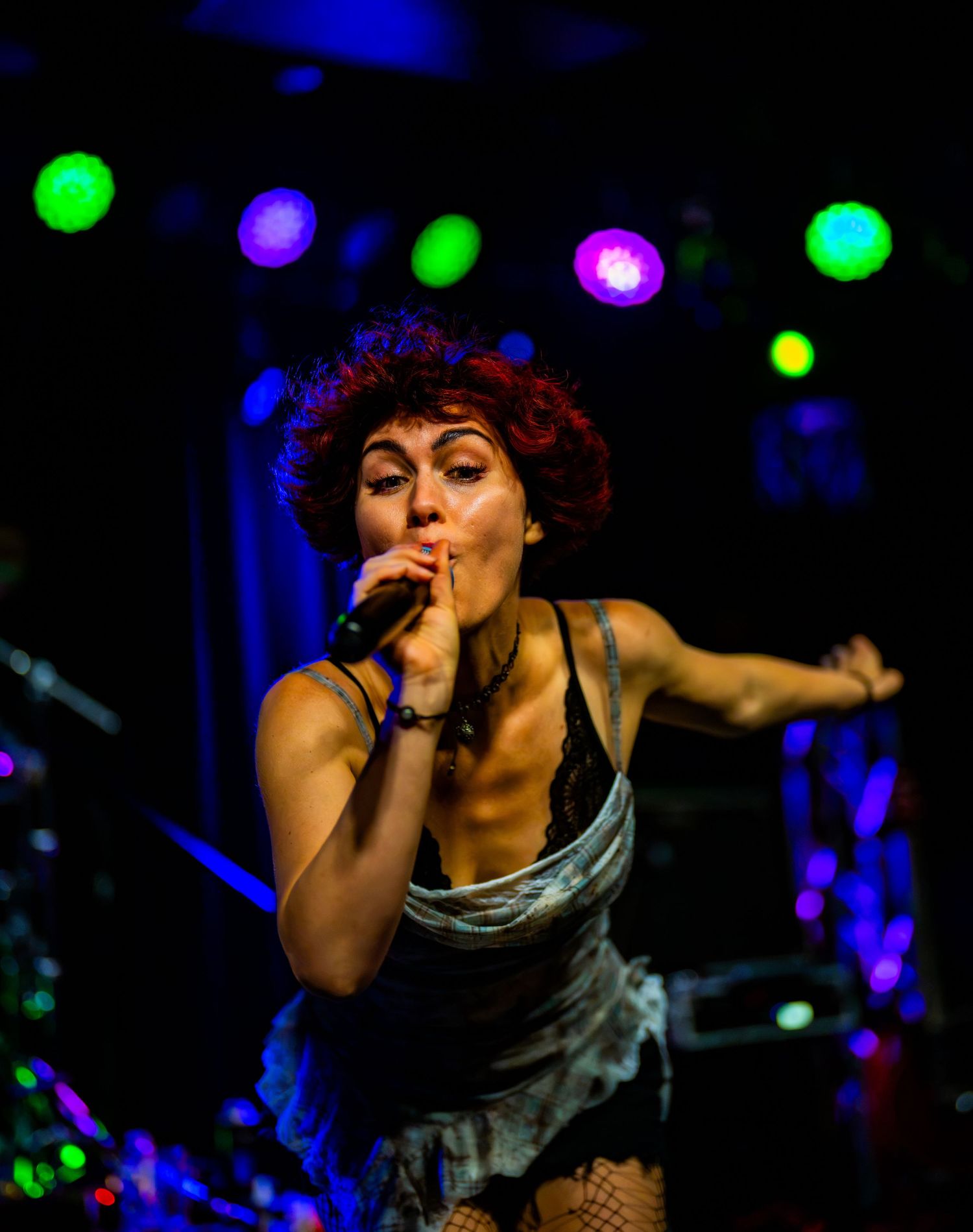 Female singer with red curly hair performs on stage holding microphone under colorful concert lights.