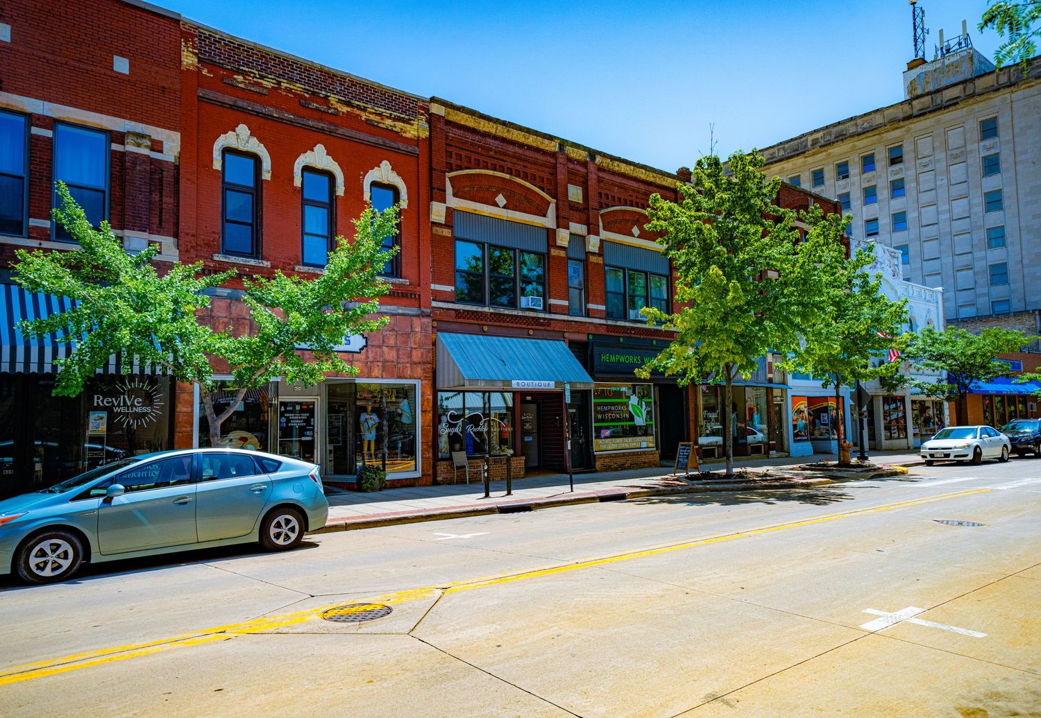Historic red brick commercial buildings with storefronts along downtown street on sunny day.