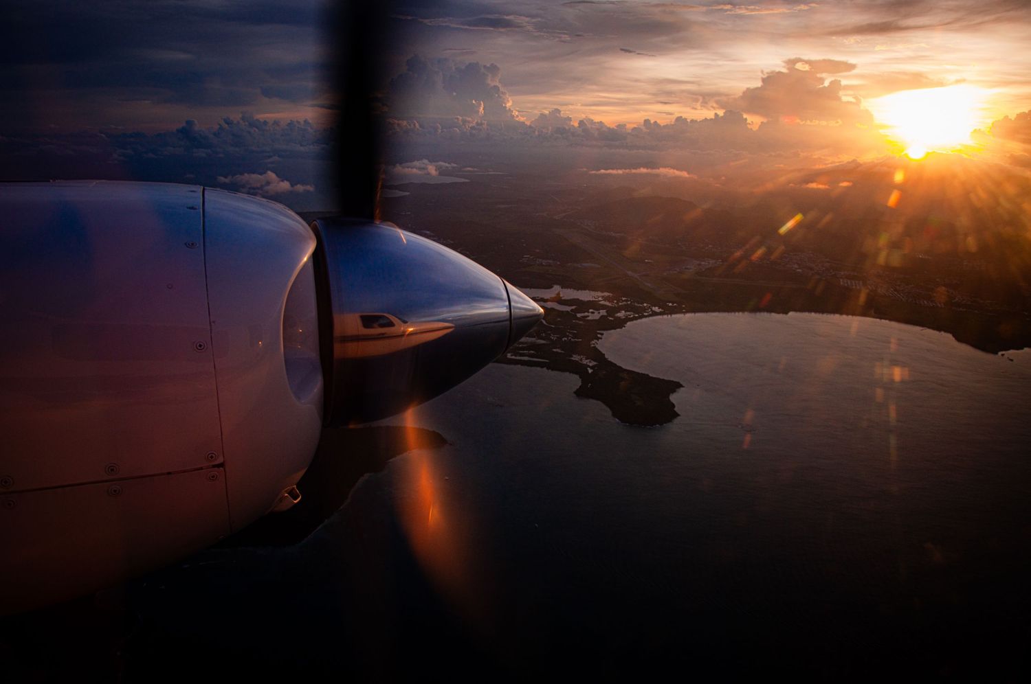 Dramatic sunset view from airplane window showing orange sky and wing silhouette.