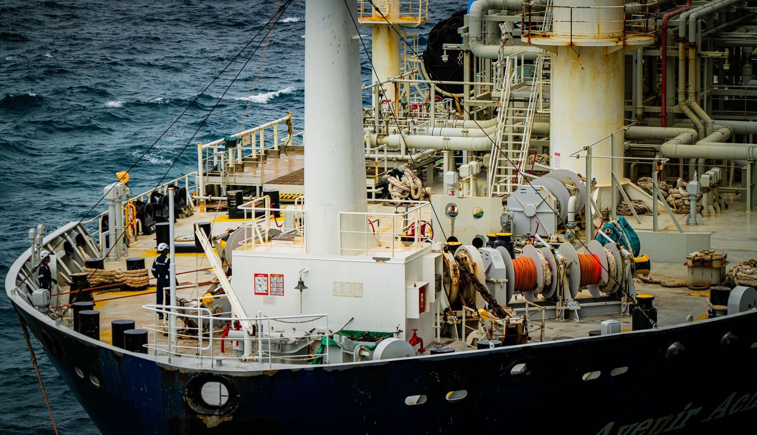 Large industrial cargo ship with cable reels and pipework on deck sailing in open ocean waters.