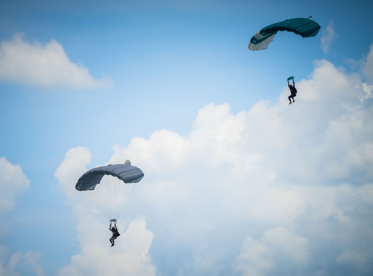Multiple skydivers floating through a bright blue sky during descent.