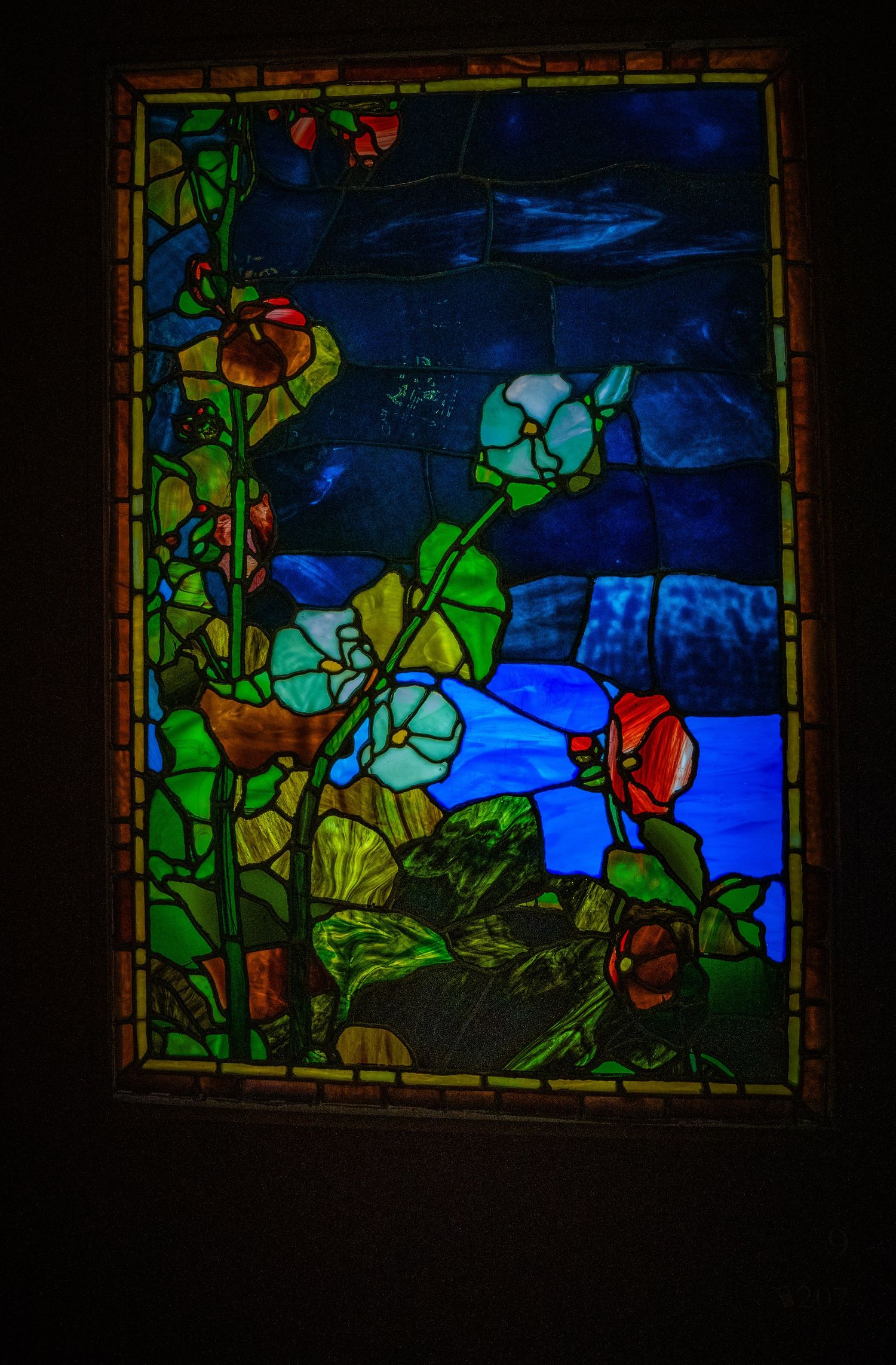 Stained glass panel showing vibrant flowers and foliage against a dark blue nighttime scene.