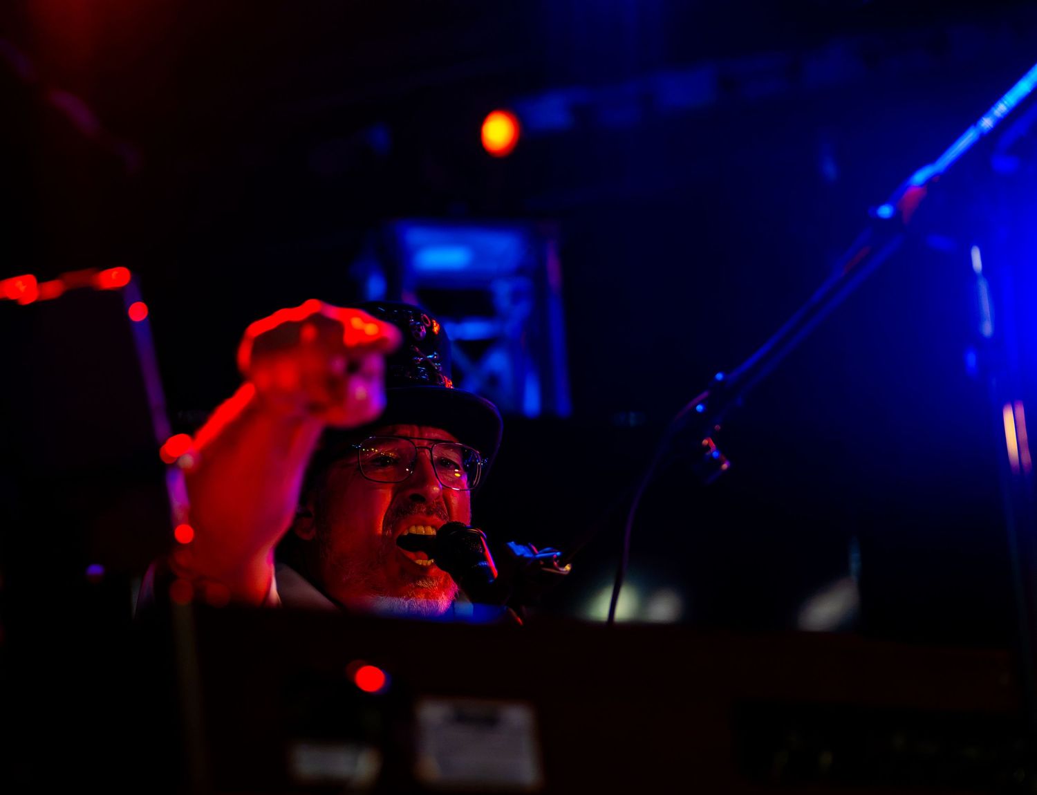 Musician performing on stage under dramatic red and blue lighting at a live concert venue.