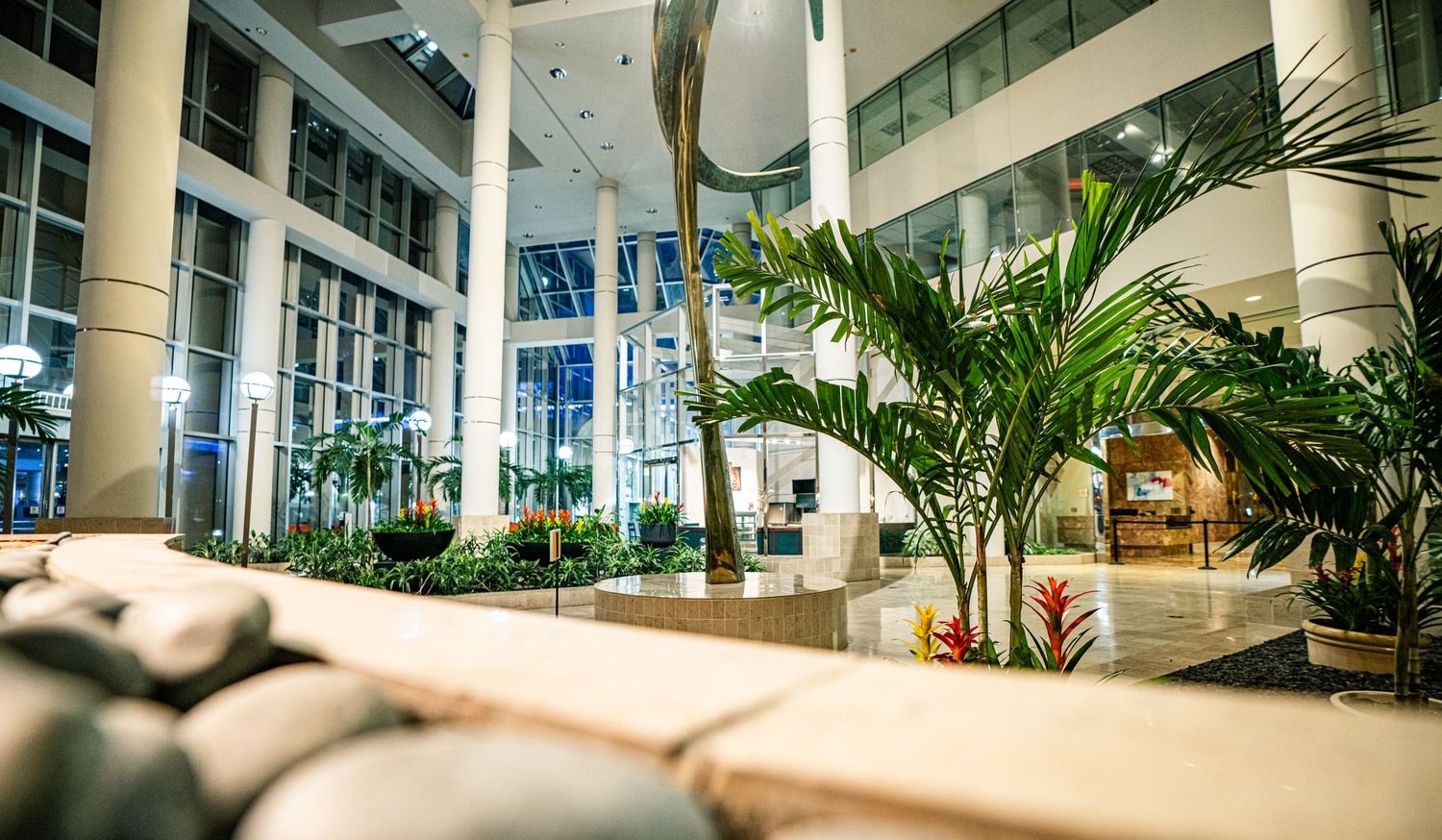 Elegant hotel lobby atrium with lush tropical palm trees, modern architecture, and bright lighting creating a luxurious atmosphere.