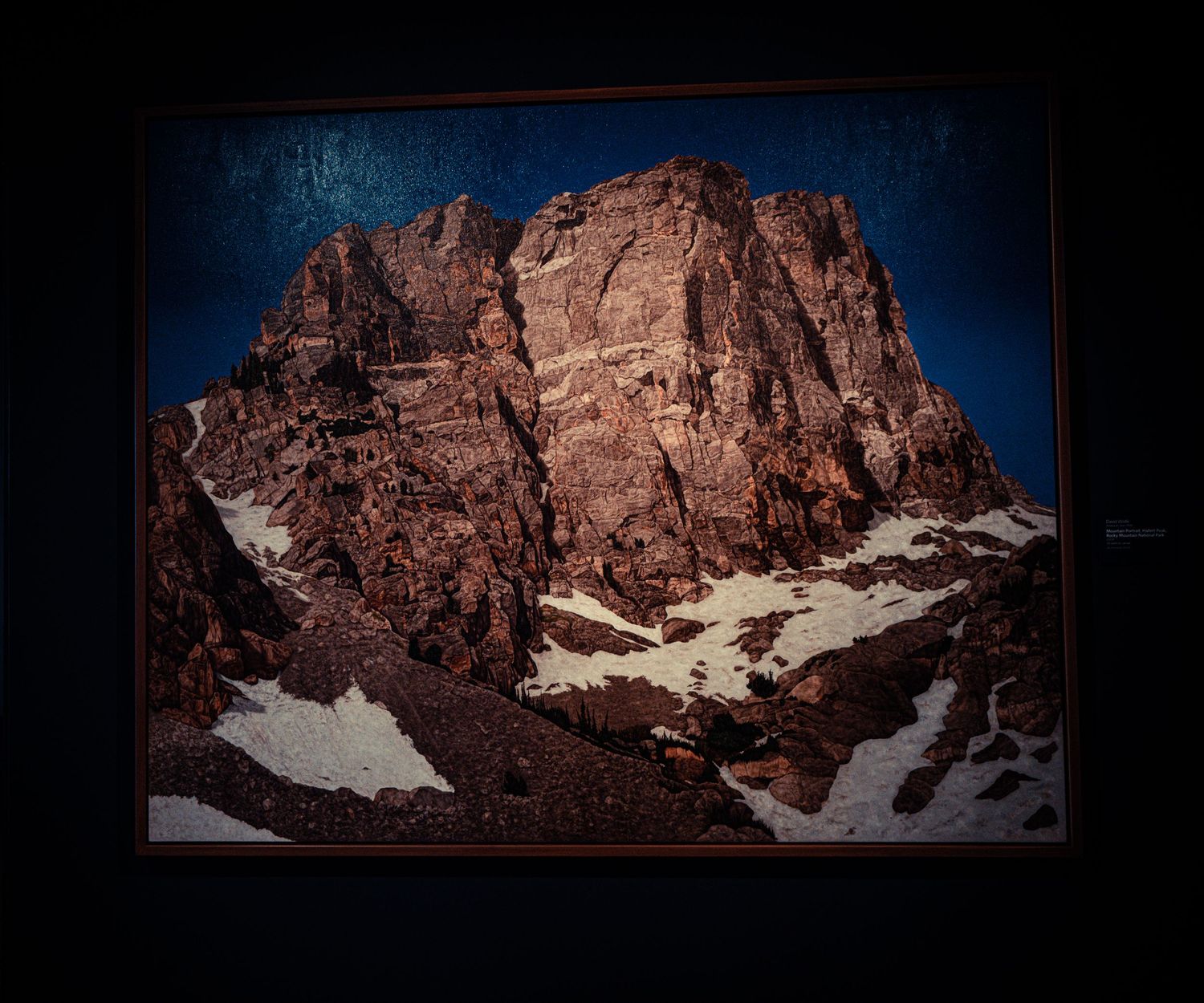 A panoramic view of rugged mountain peaks with patches of snow against a dark dramatic sky.
