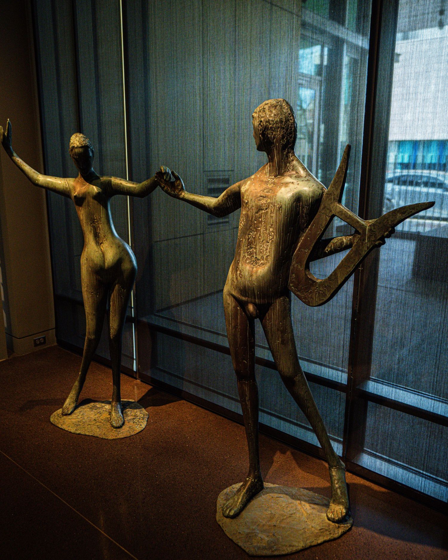 Bronze sculpture of an athletic figure in dynamic motion displayed in a museum gallery with dark lighting.