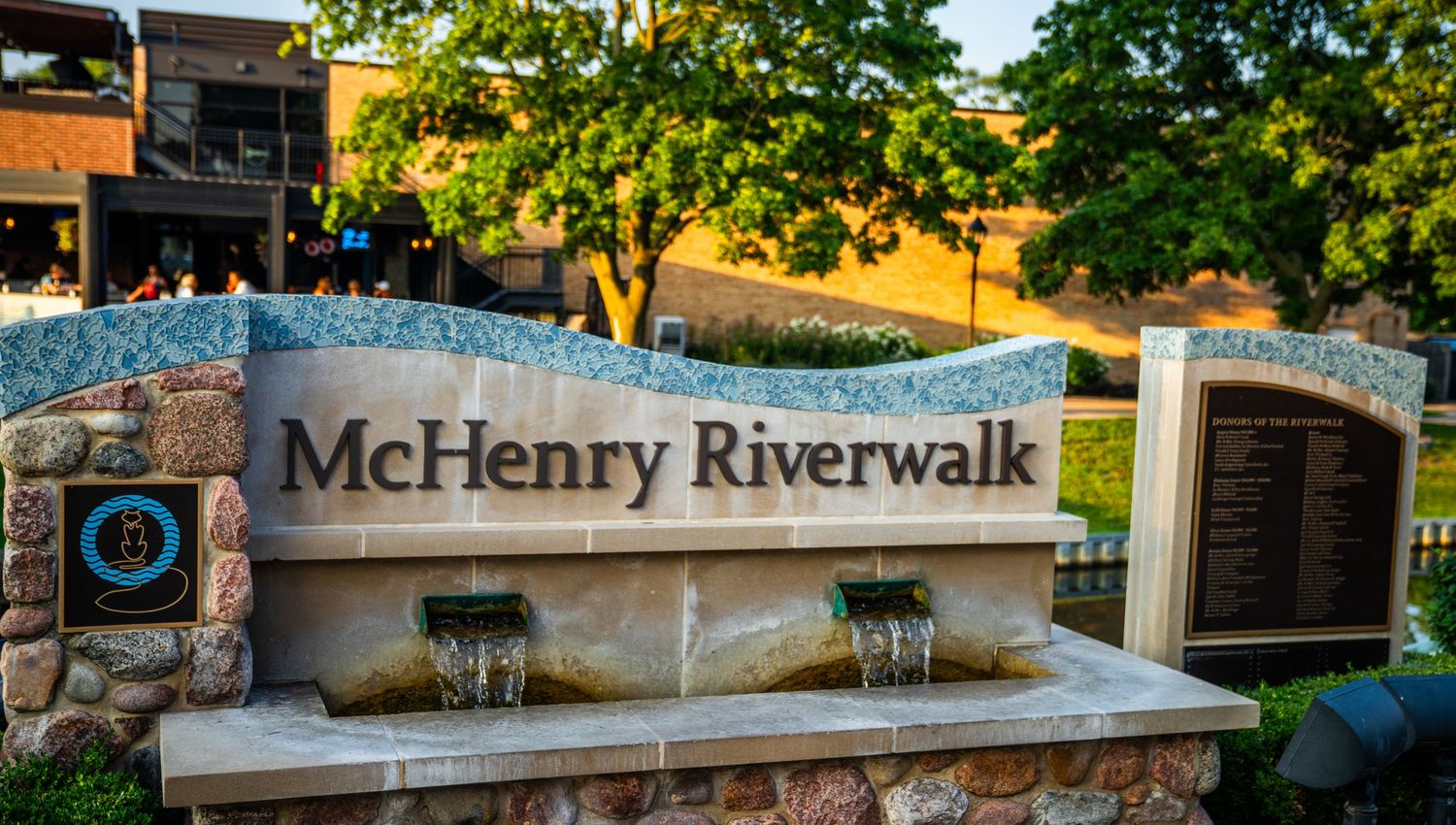Stone entrance sign for McHenry Riverwalk with water feature and landscaping.