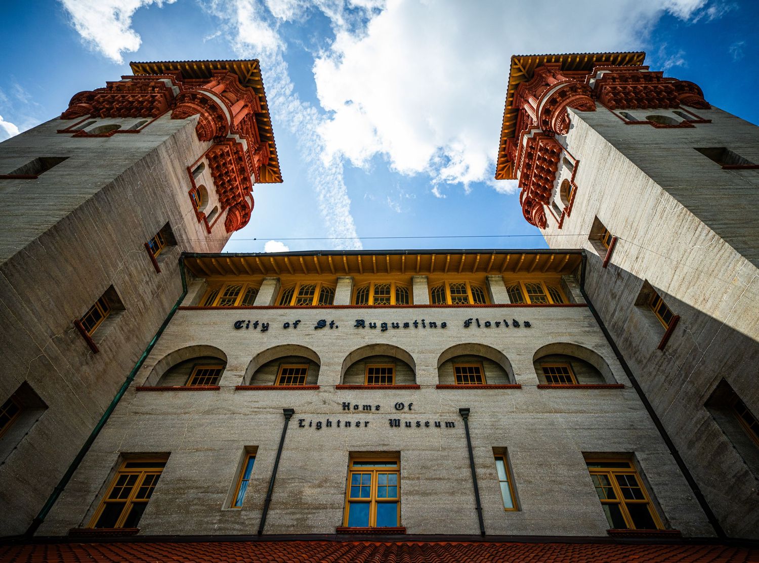 Low angle view of ornate brick building facade with blue sky and white clouds.