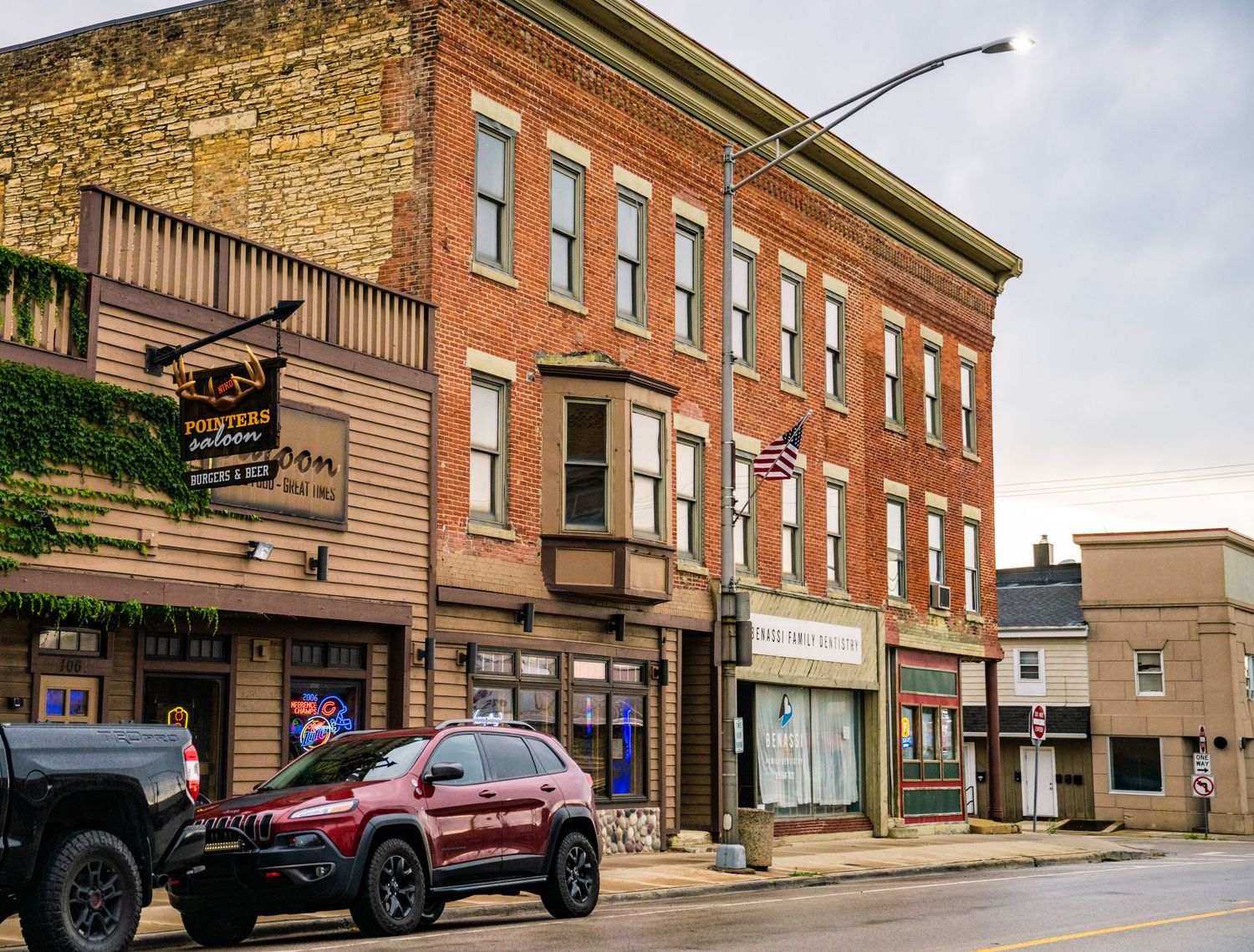 Historic red brick commercial buildings along a small town main street with parked vehicles.