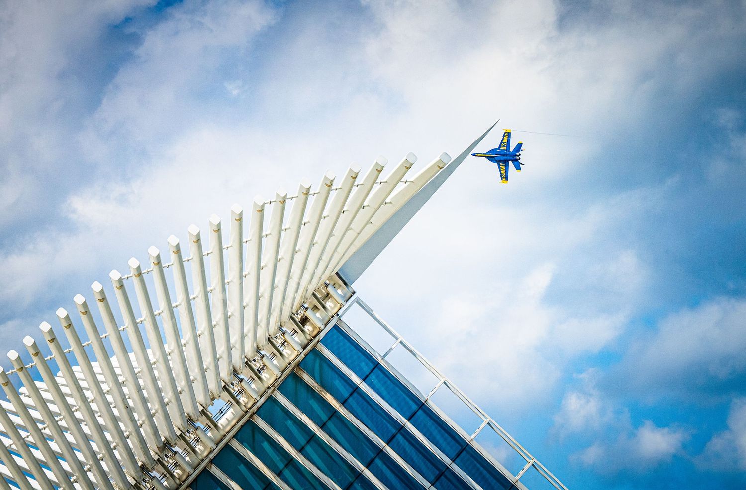 Modern architectural detail with white ribbed structure as planes fly overhead against cloudy sky.