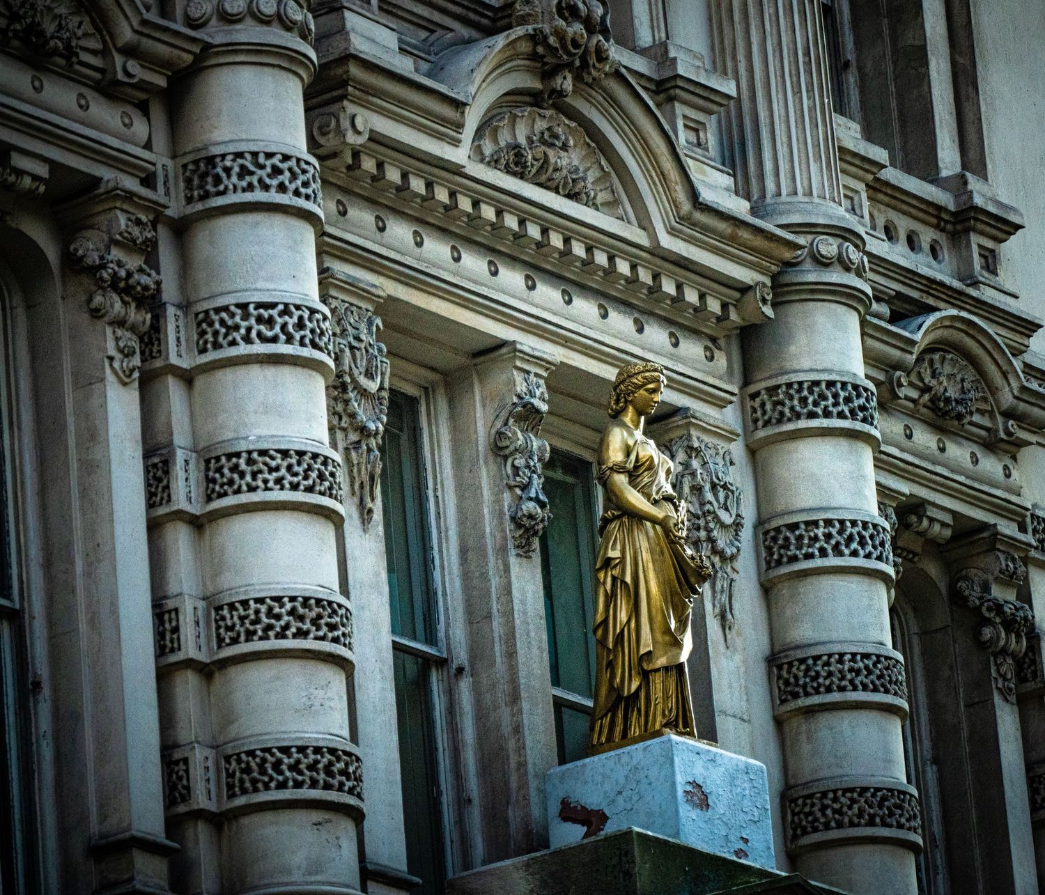 Neoclassical building exterior with decorated columns and golden statue details.