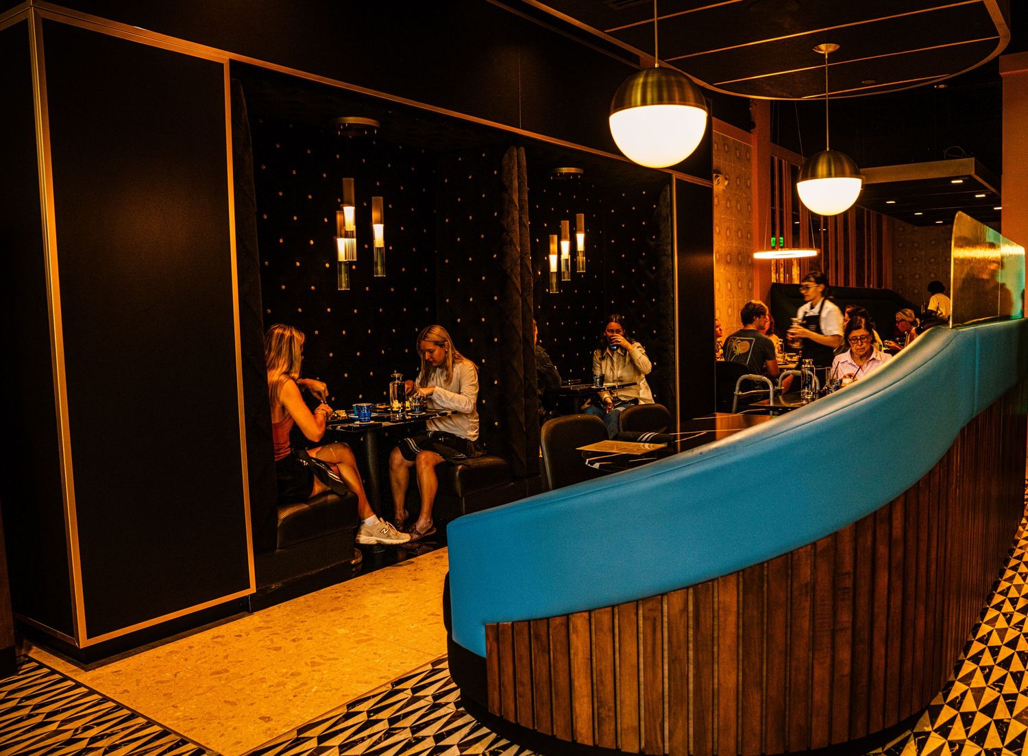 Trendy bar area with turquoise accents and warm lighting features geometric black and white flooring.