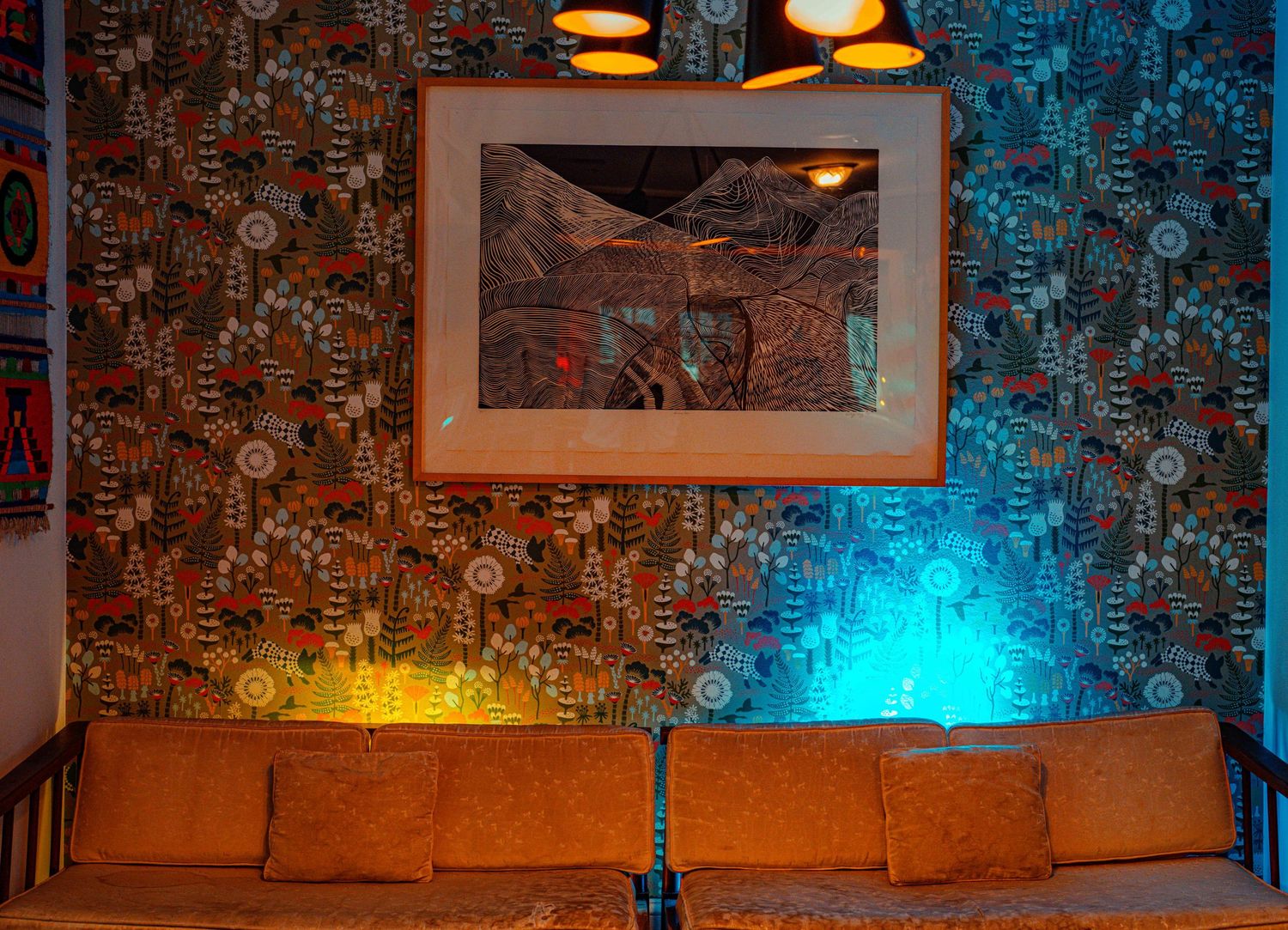 Orange couch against patterned wallpaper with framed artwork and ambient lighting creating a cozy lounge atmosphere.