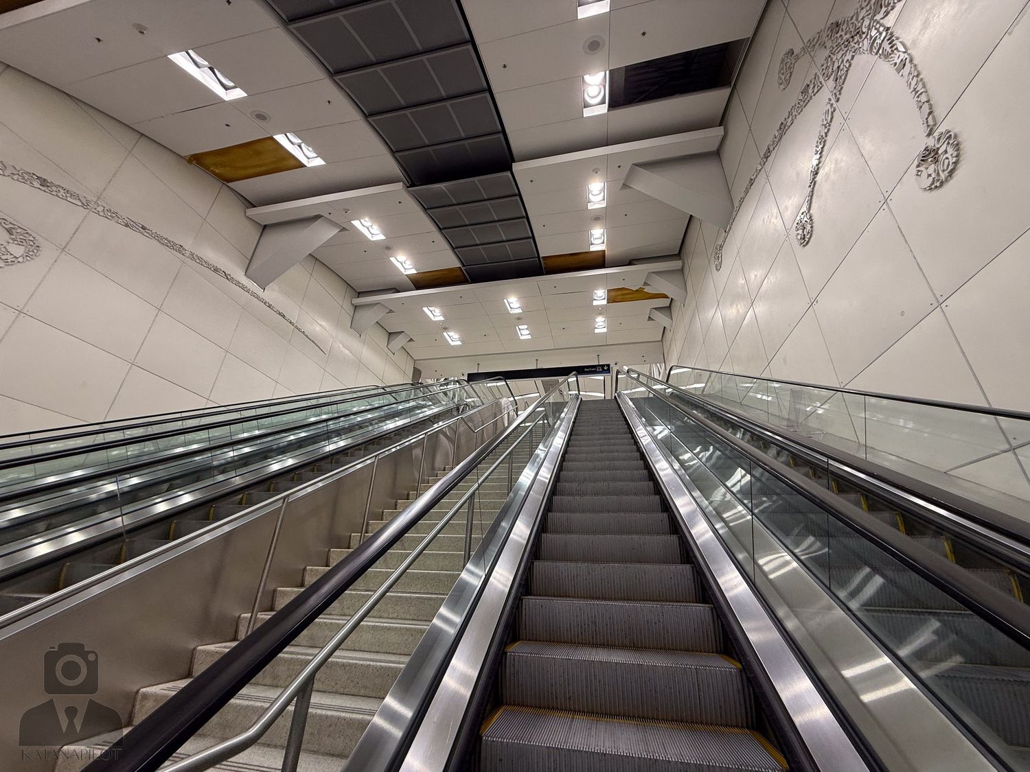 Modern escalator with bright lighting in white-tiled corridor.