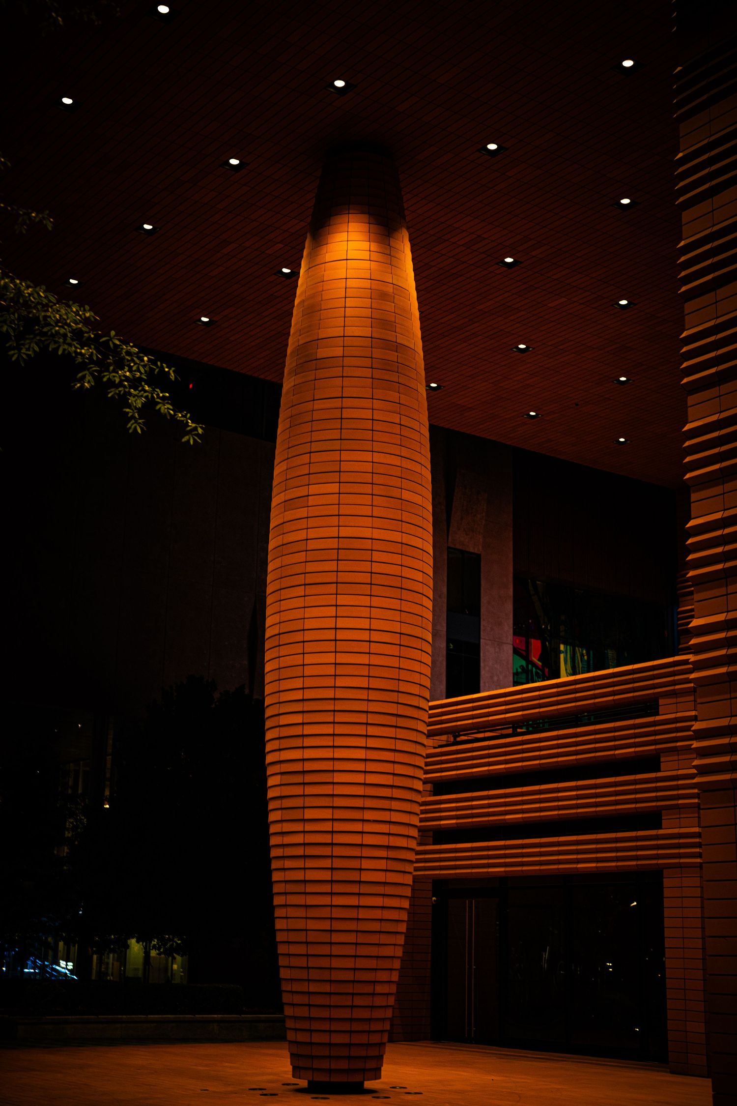 Large illuminated cylindrical light fixture mounted on wall in modern interior space.