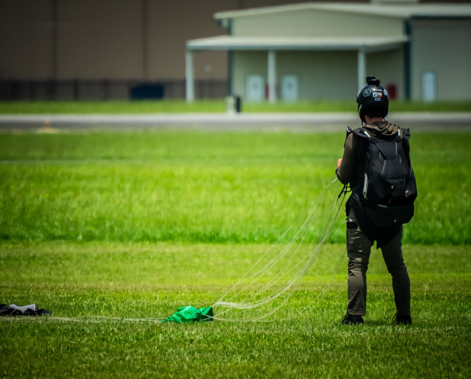 Parachutist preparing landing gear on grassy field during training exercise.