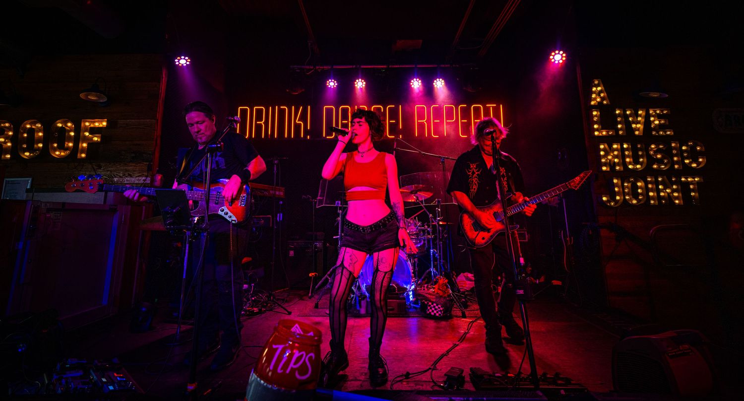 Concert stage lit with purple and pink lights showing musical performers and equipment.