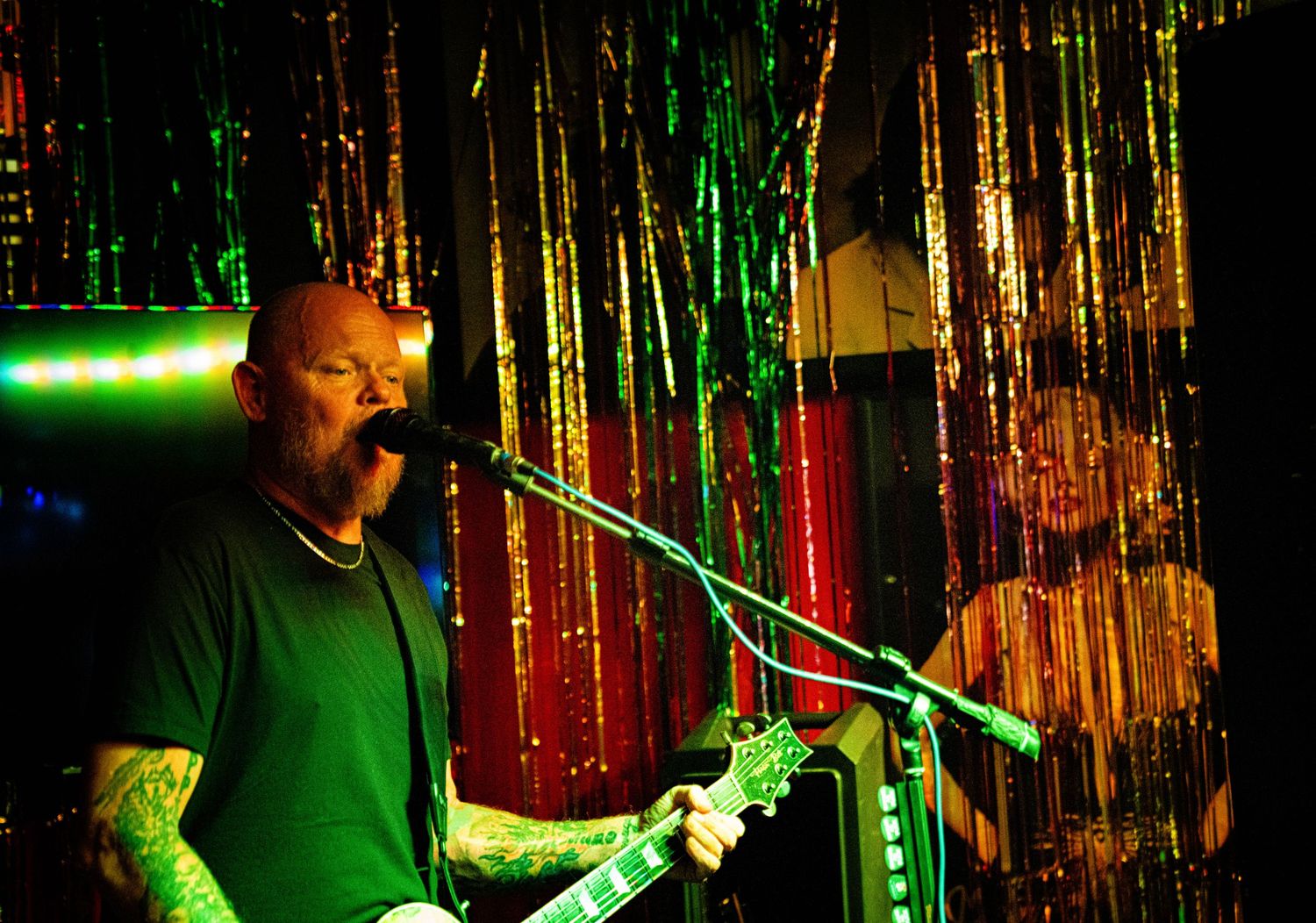 Guitar player performs against a backdrop of metallic streamers with green lighting effects.